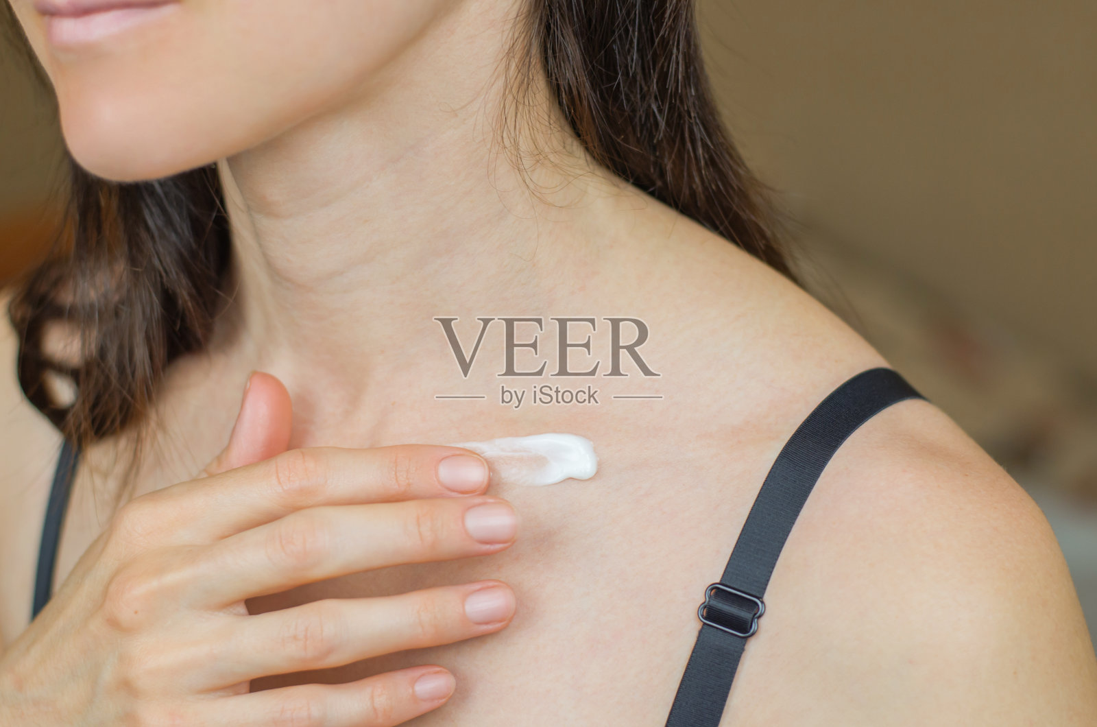 一个女人在锁骨上涂润肤霜的特写。女士在身体上涂抹润肤霜照片摄影图片