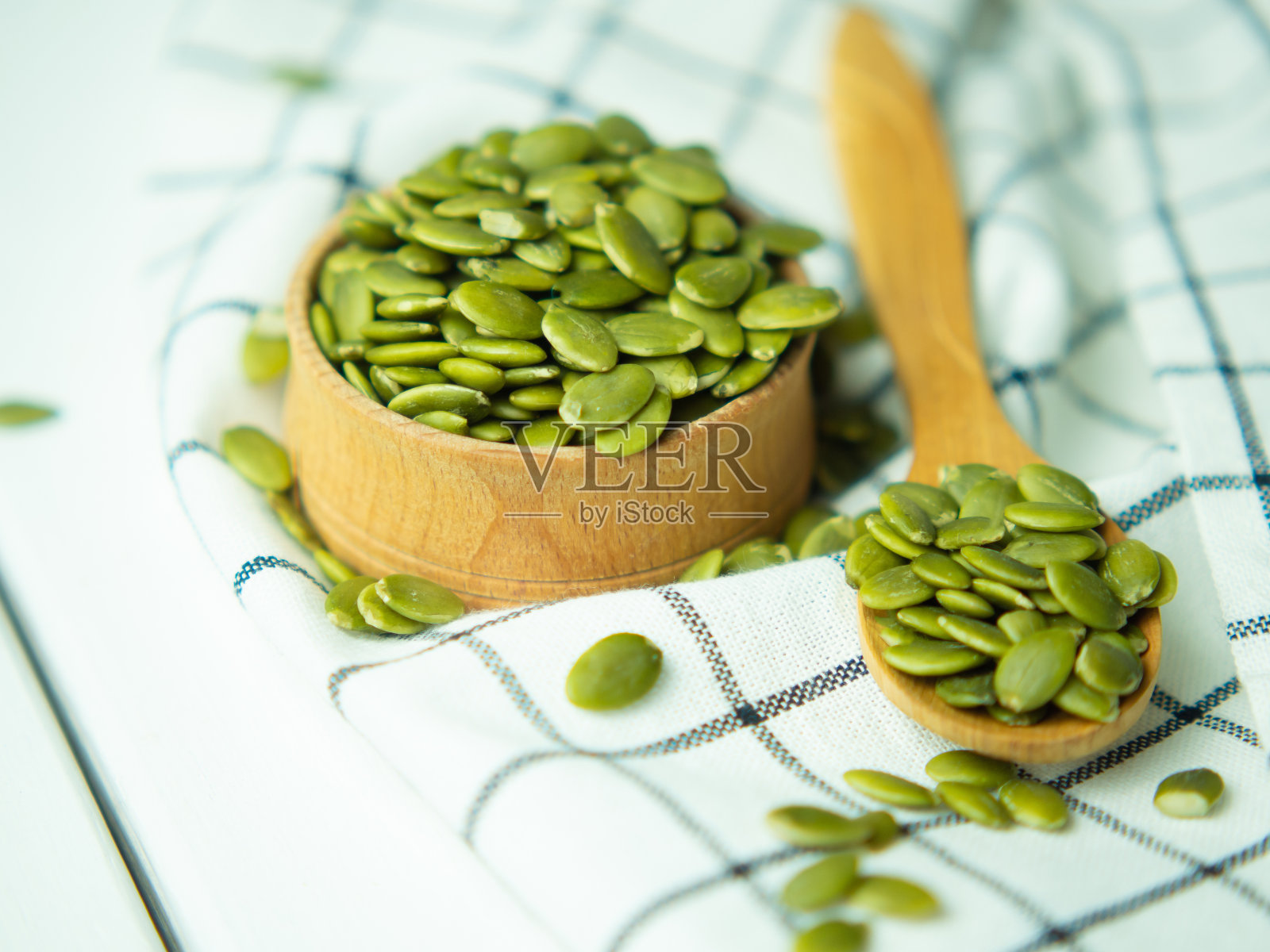 白色的木桌上放着满满一碗一勺的南瓜子。照片摄影图片