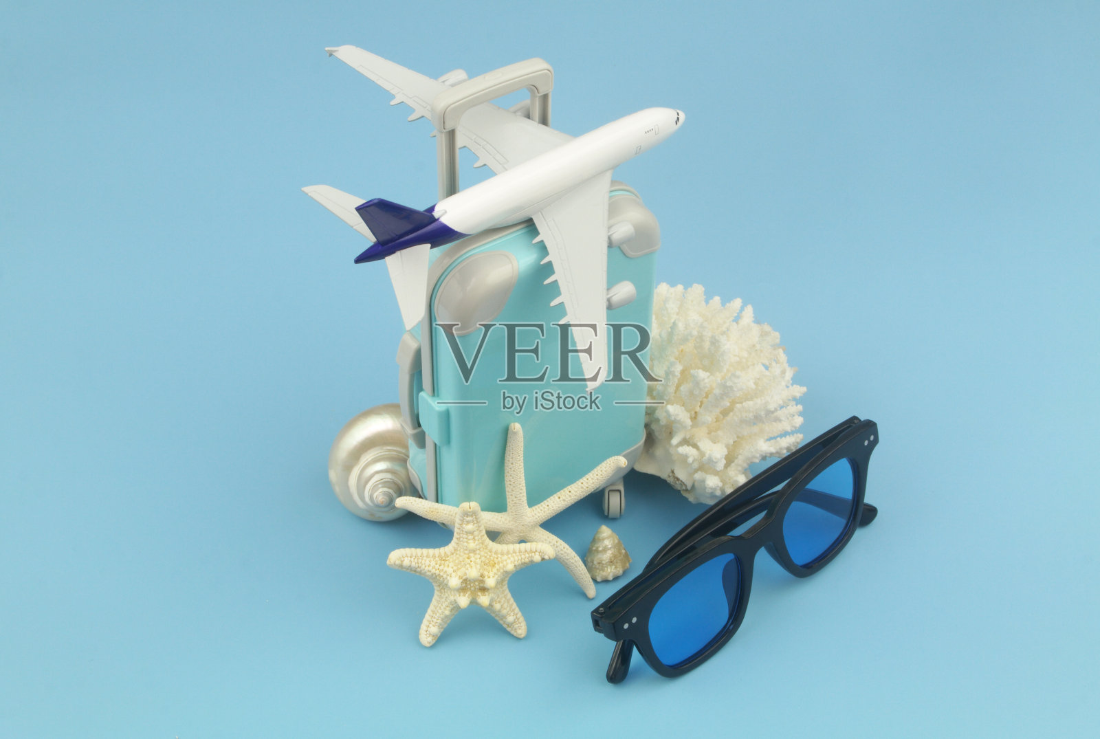 飞机模型行李箱和太阳镜与海星和珊瑚在蓝色背景。照片摄影图片