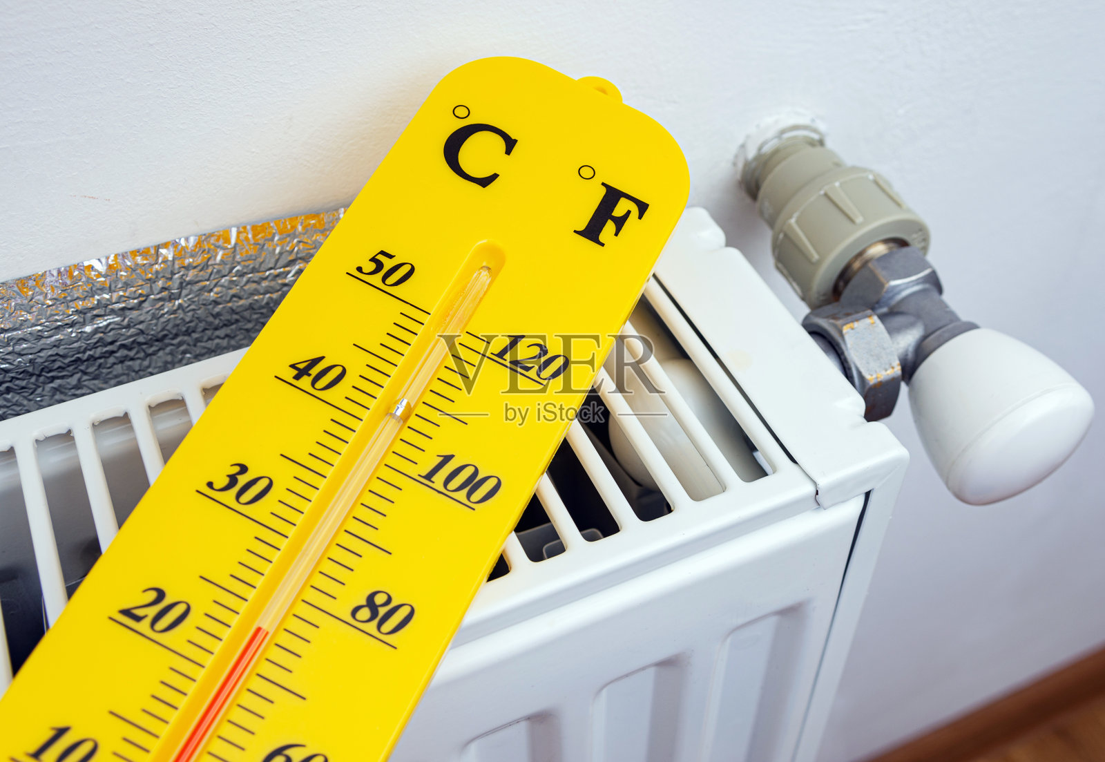 黄色温度计与摄氏度和华氏度附近的暖气散热器。照片摄影图片