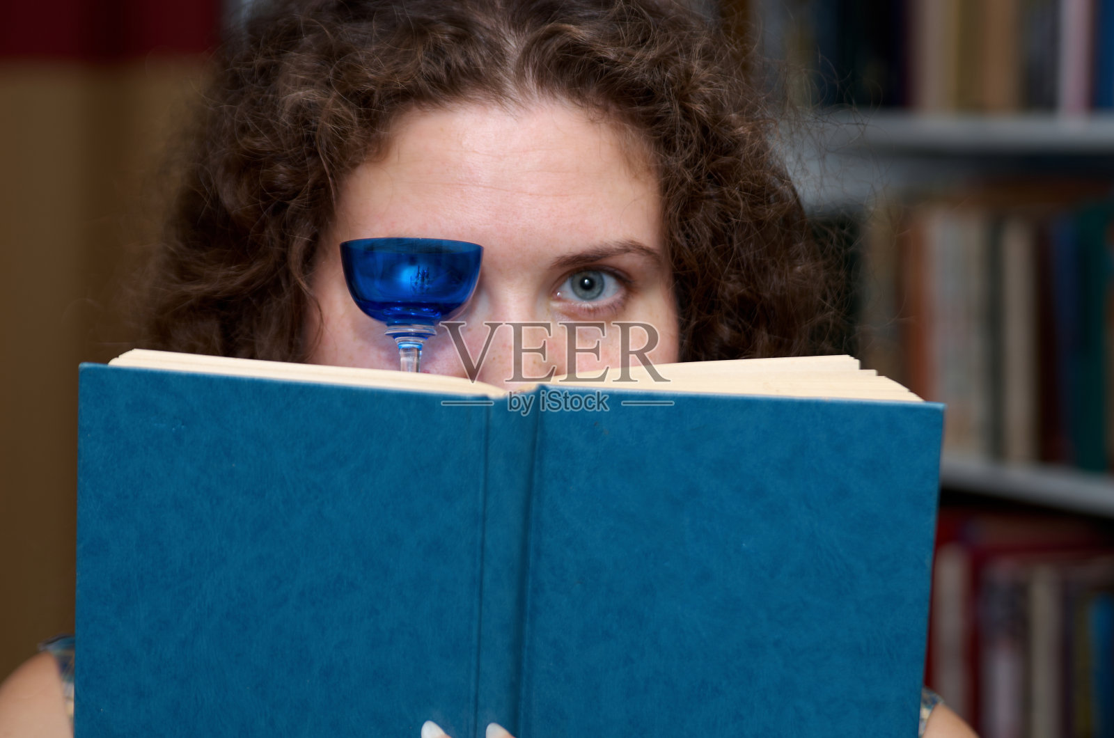 在书柜的背景上，一位手持玻璃杯的妇女正在读书照片摄影图片