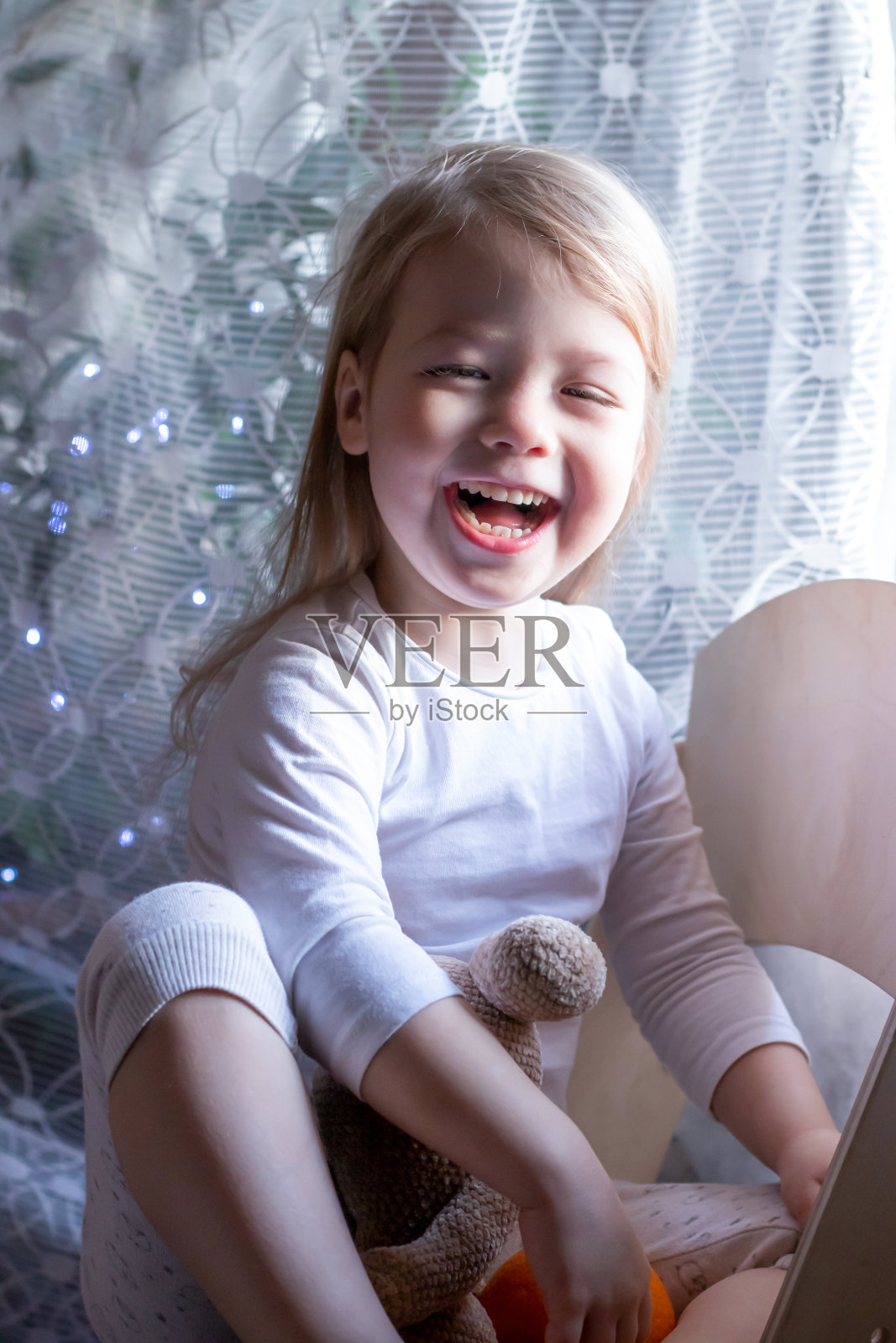 画像的笑金发女孩坐在椅子上的背景圣诞彩灯照片摄影图片