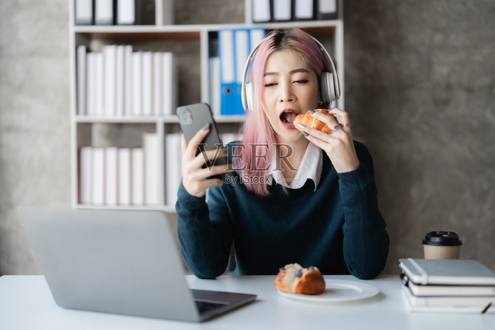 年轻兴奋的亚洲妇女戴着耳机正在玩他的智能手机。玩家与互联网照片摄影图片