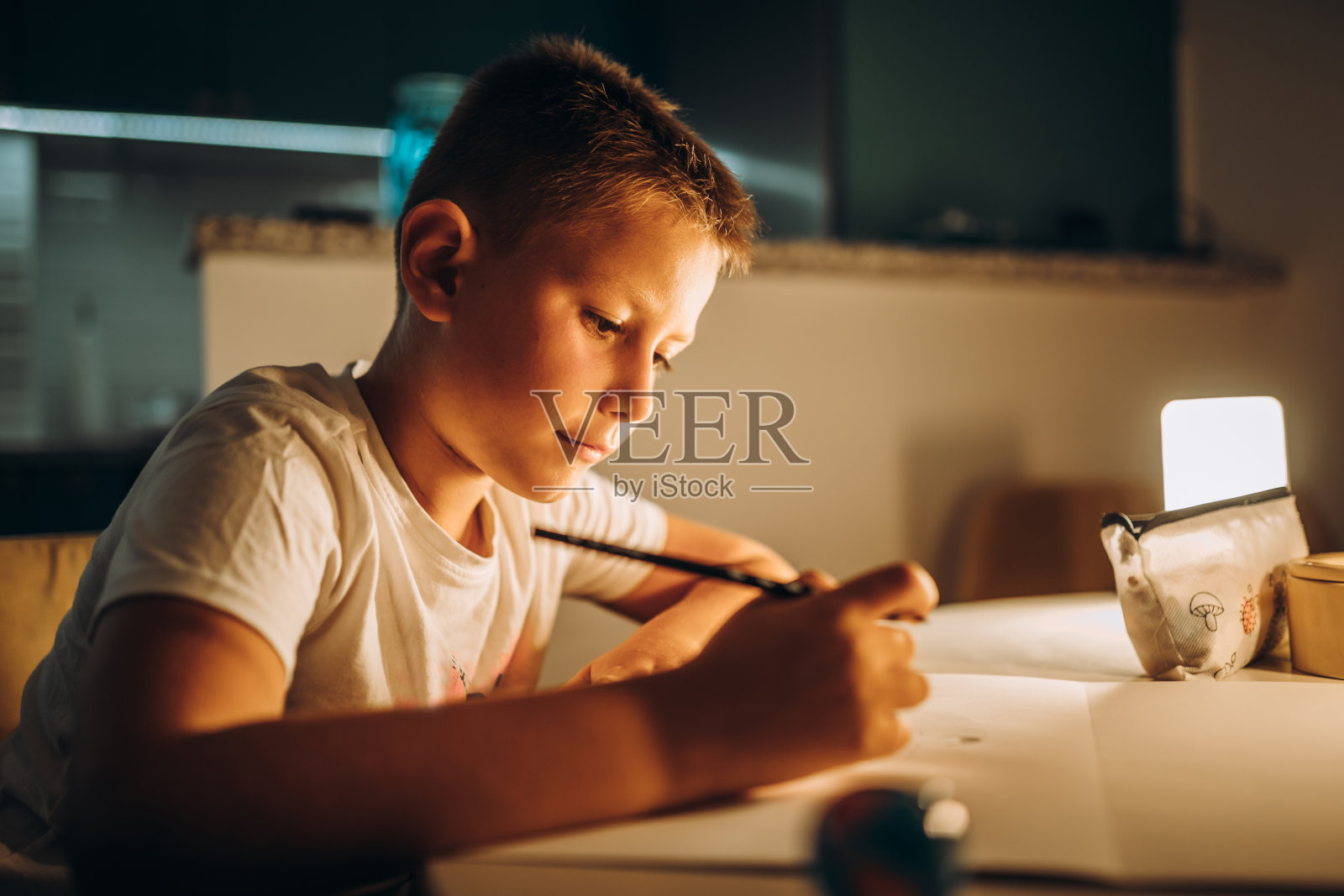 孩子拿着笔在昏暗的灯光下写字/画画照片摄影图片