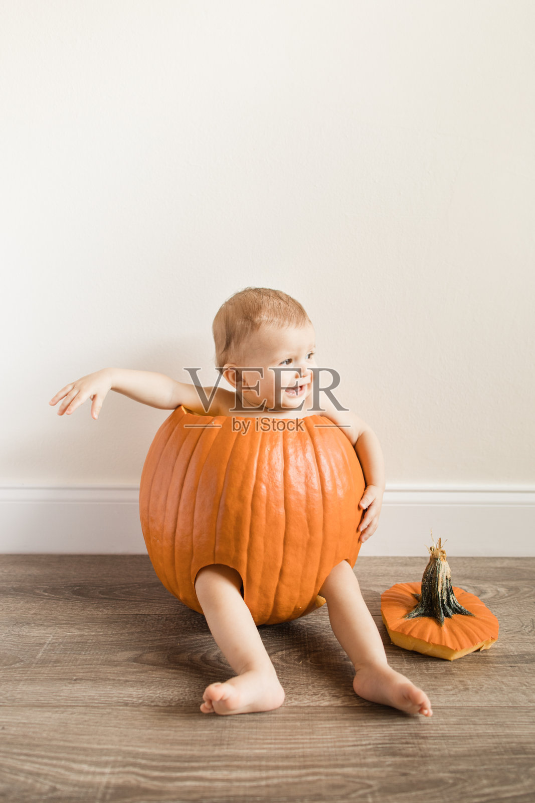 2022年秋天，一个可爱的10个月大的男婴坐在一个真正的橙色南瓜里，腿和胳膊在家里的地板上照片摄影图片