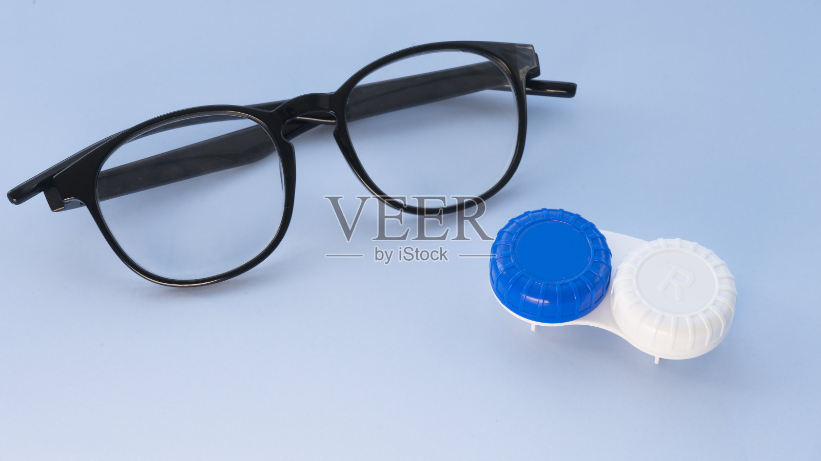 浅蓝色背景的眼镜和隐形眼镜容器照片摄影图片