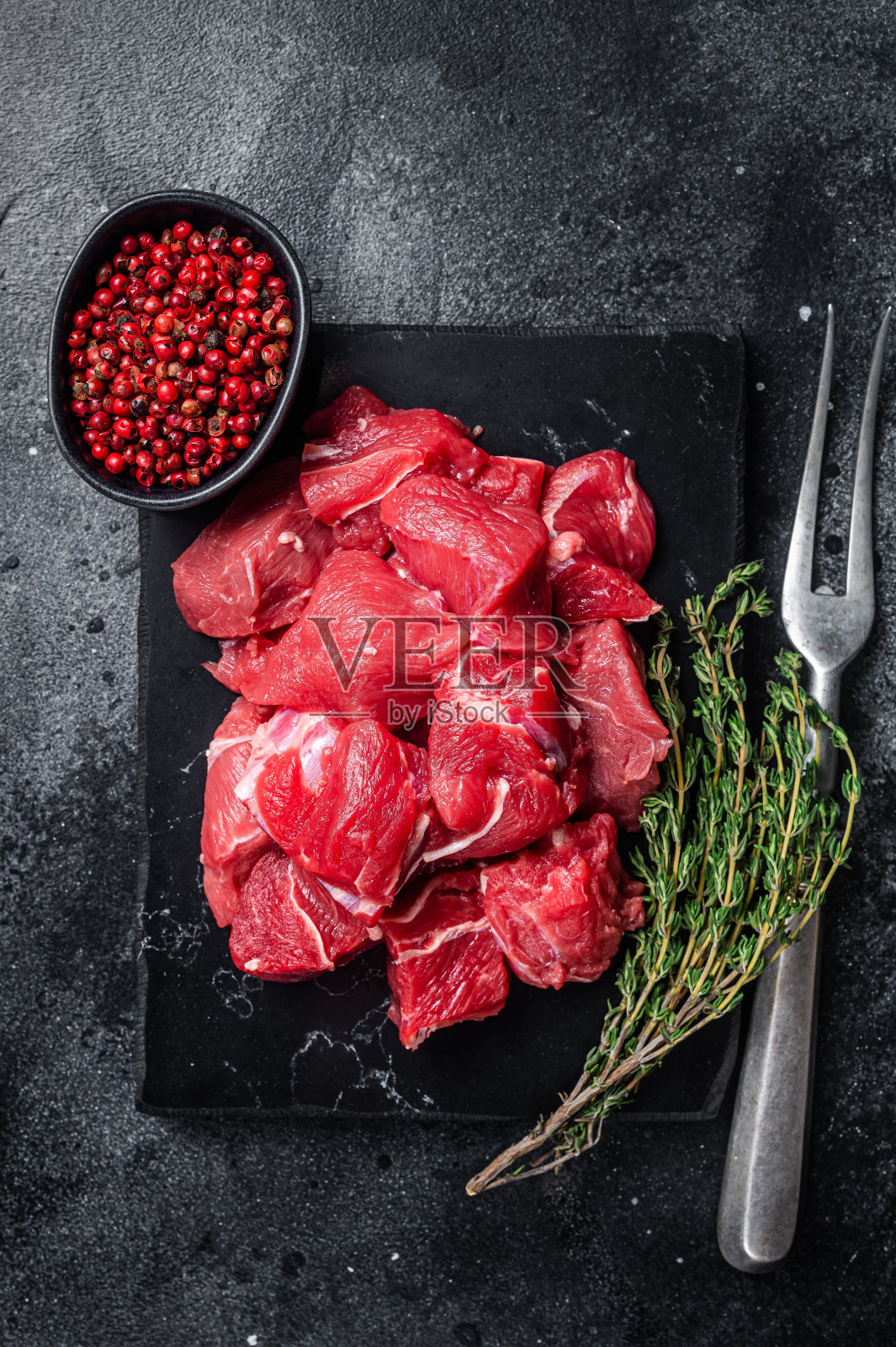 大理石板上炖牛肉用的生红牛肉丁。黑色背景。俯视图照片摄影图片