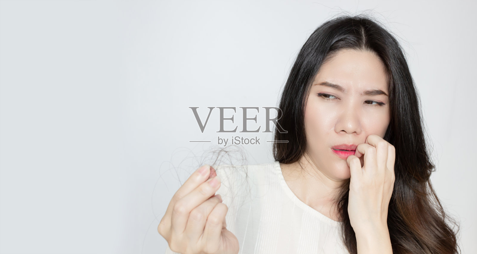 亚洲美女正用手寻找她的脱发，抬起另一只手摸在嘴唇上，露出震惊和担心的表情。照片摄影图片