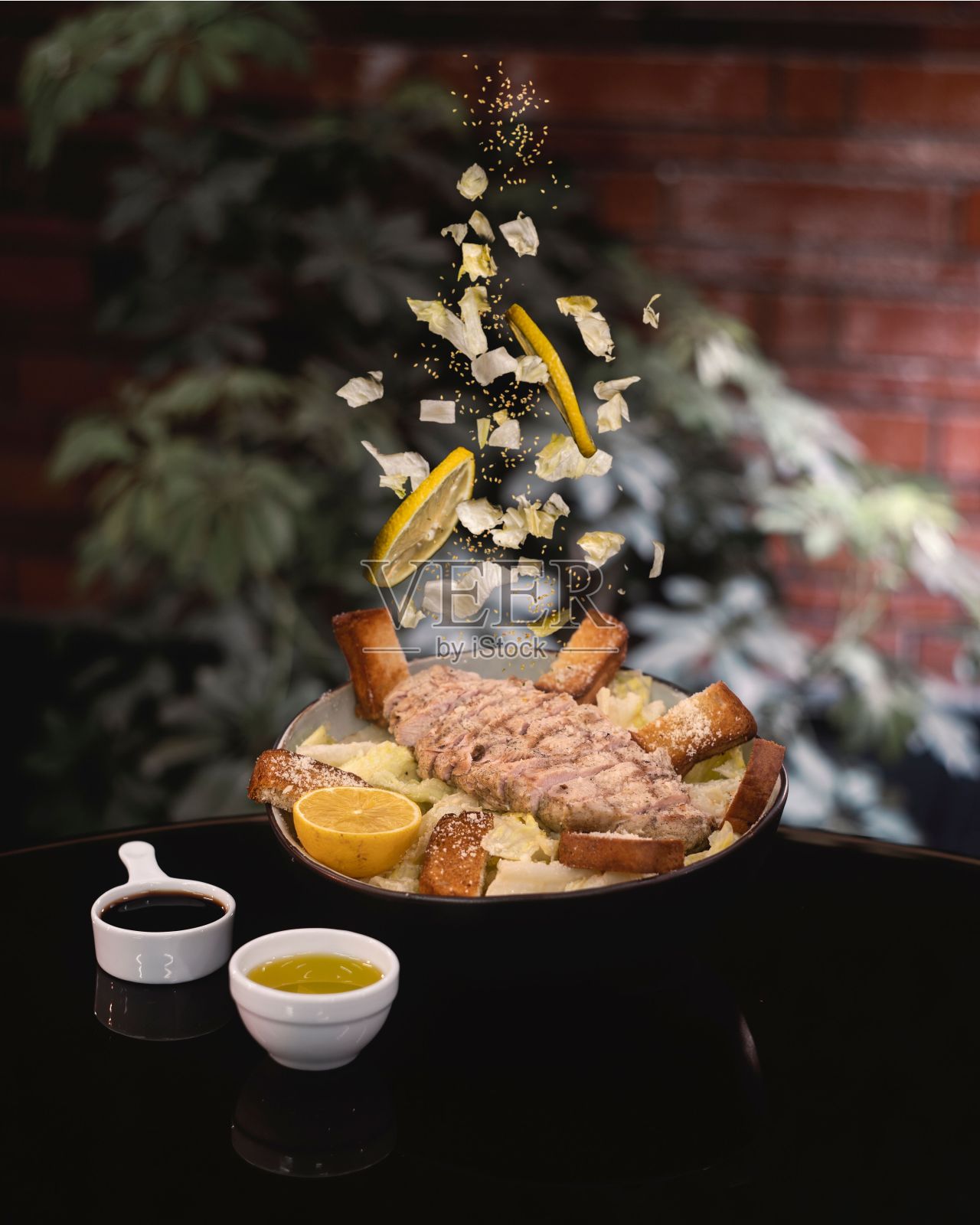 垂直拍摄的凯撒沙拉和酱汁在黑色的桌子上，顶部的配料正在掉落照片摄影图片