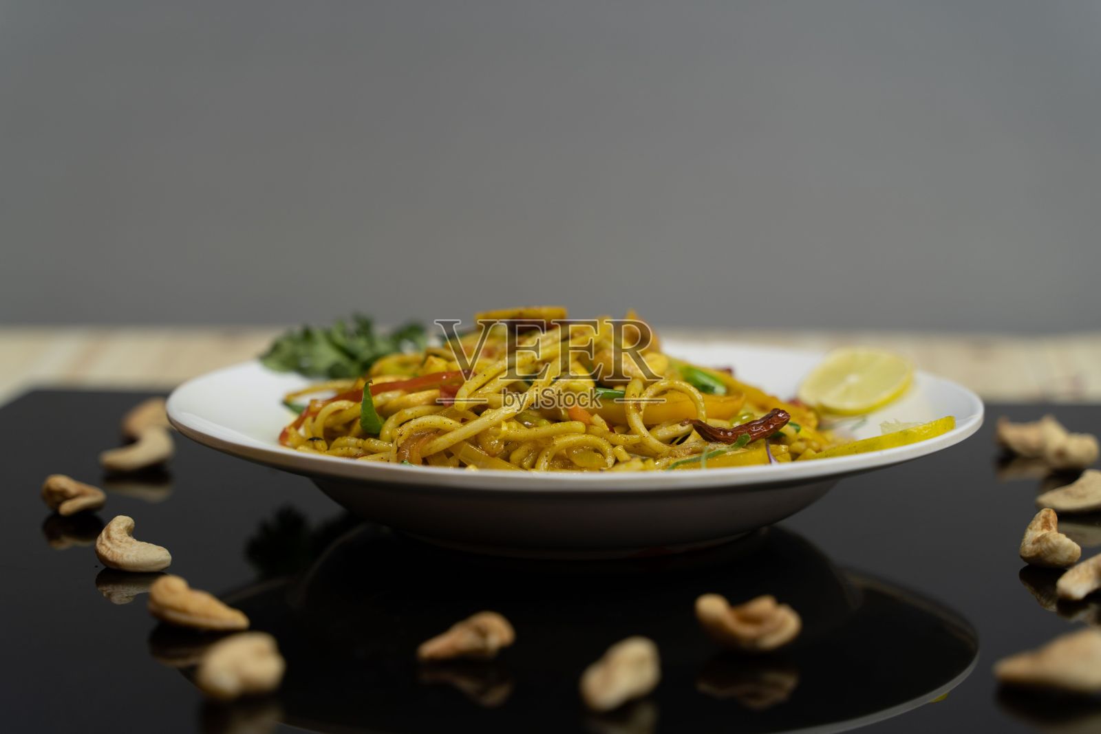 黑色的桌子上，白色的盘子里盛满了美味的面条和腰果照片摄影图片