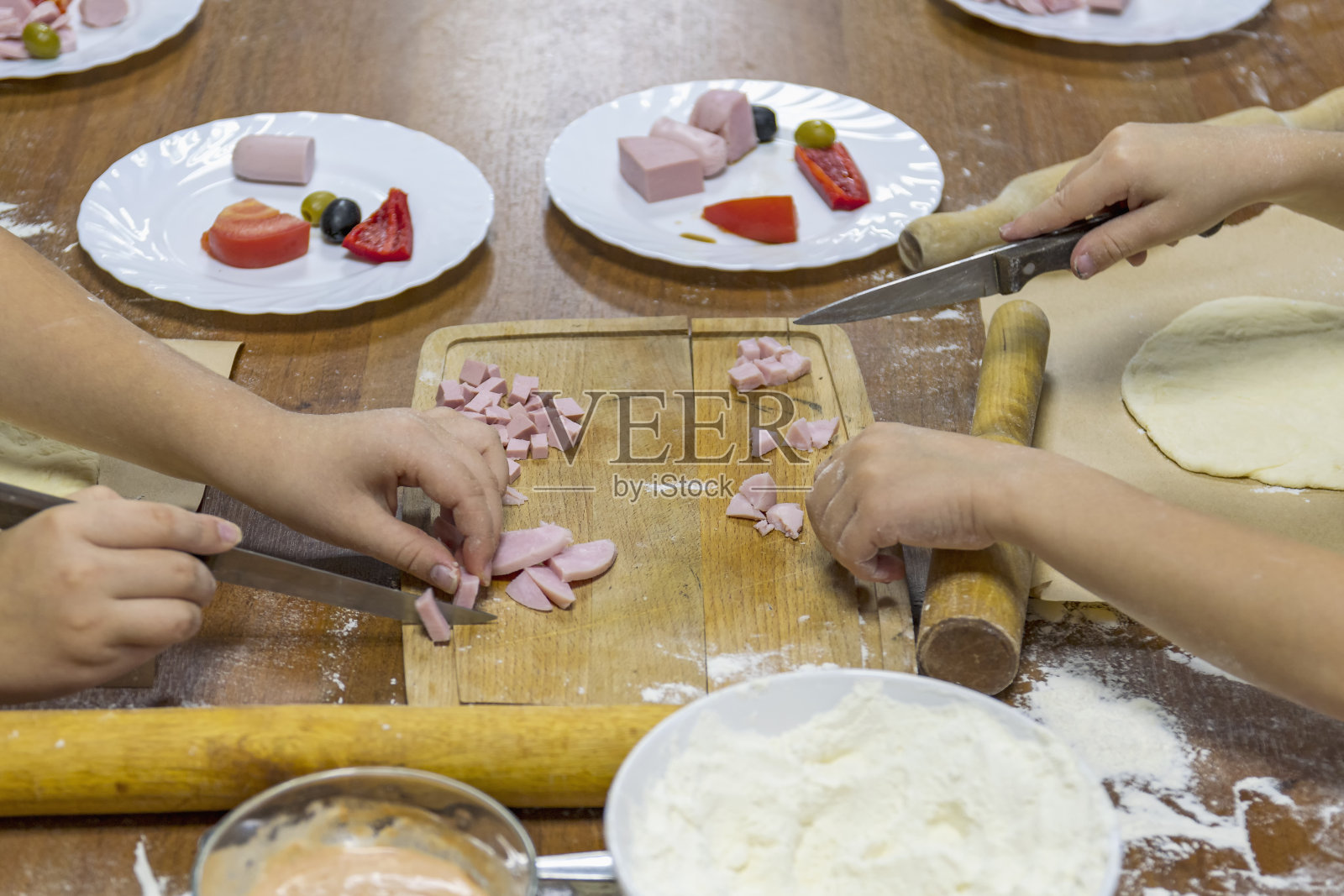 剪短的孩子们的手在木制砧板上切香肠。旁边是未来菜肴的食材照片摄影图片