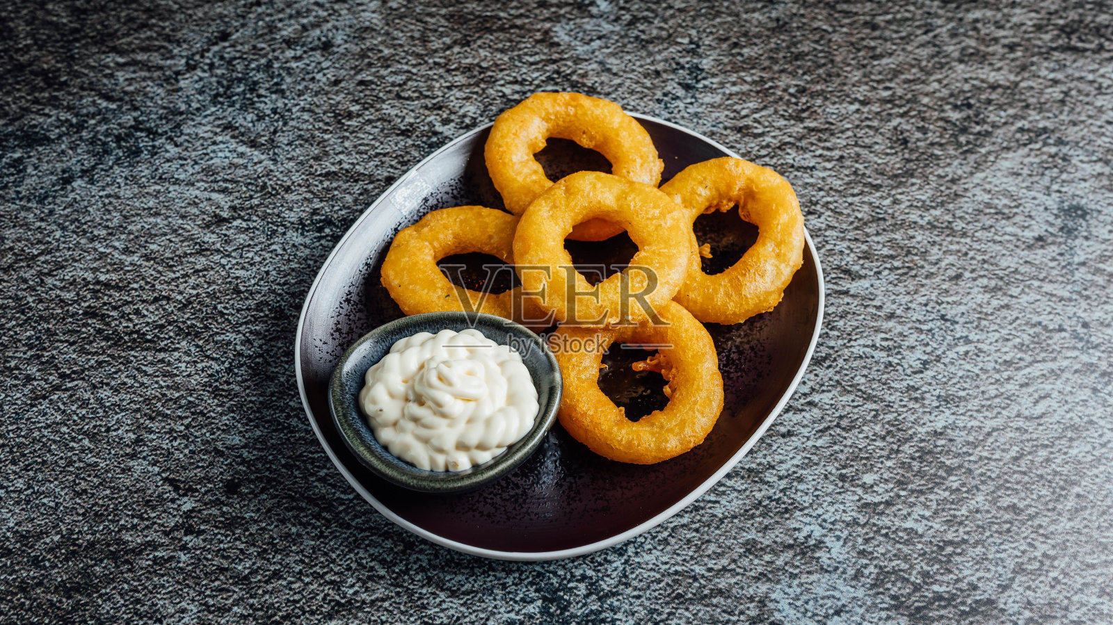 俯视图的金色洋葱圈与奶油酱汁供应在一个圆托盘照片摄影图片