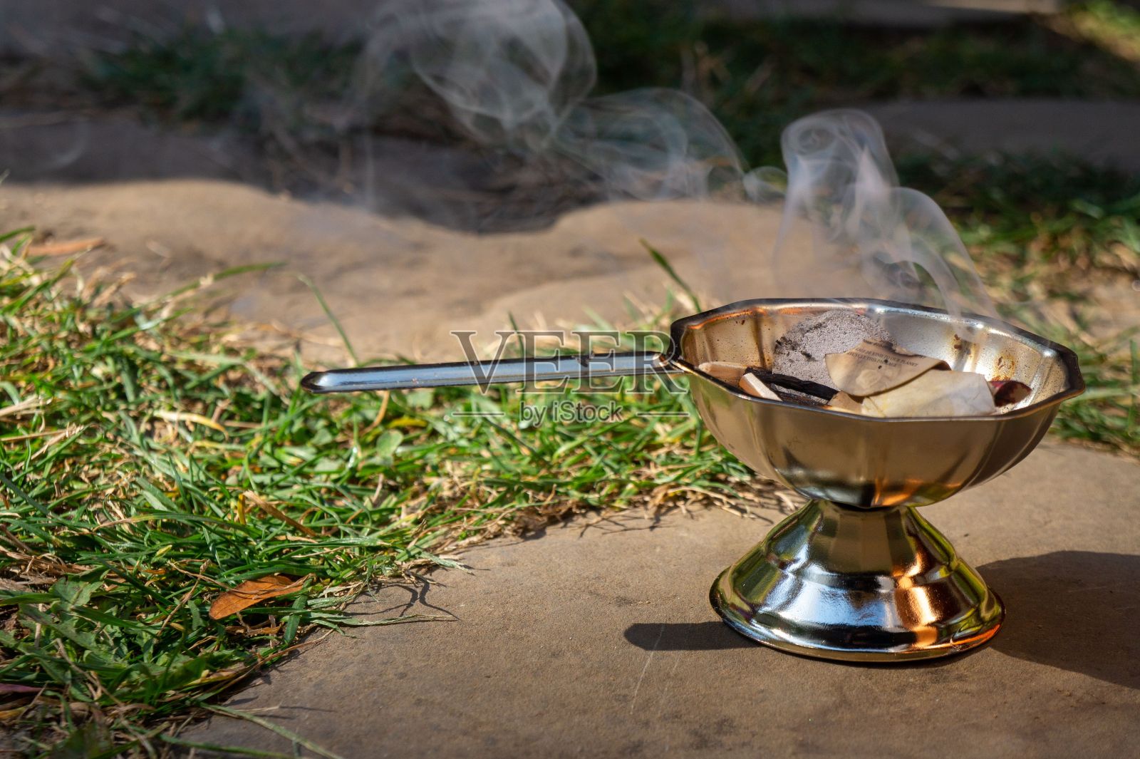 在草地上，灰烬在不锈钢碗里燃烧的特写照片摄影图片