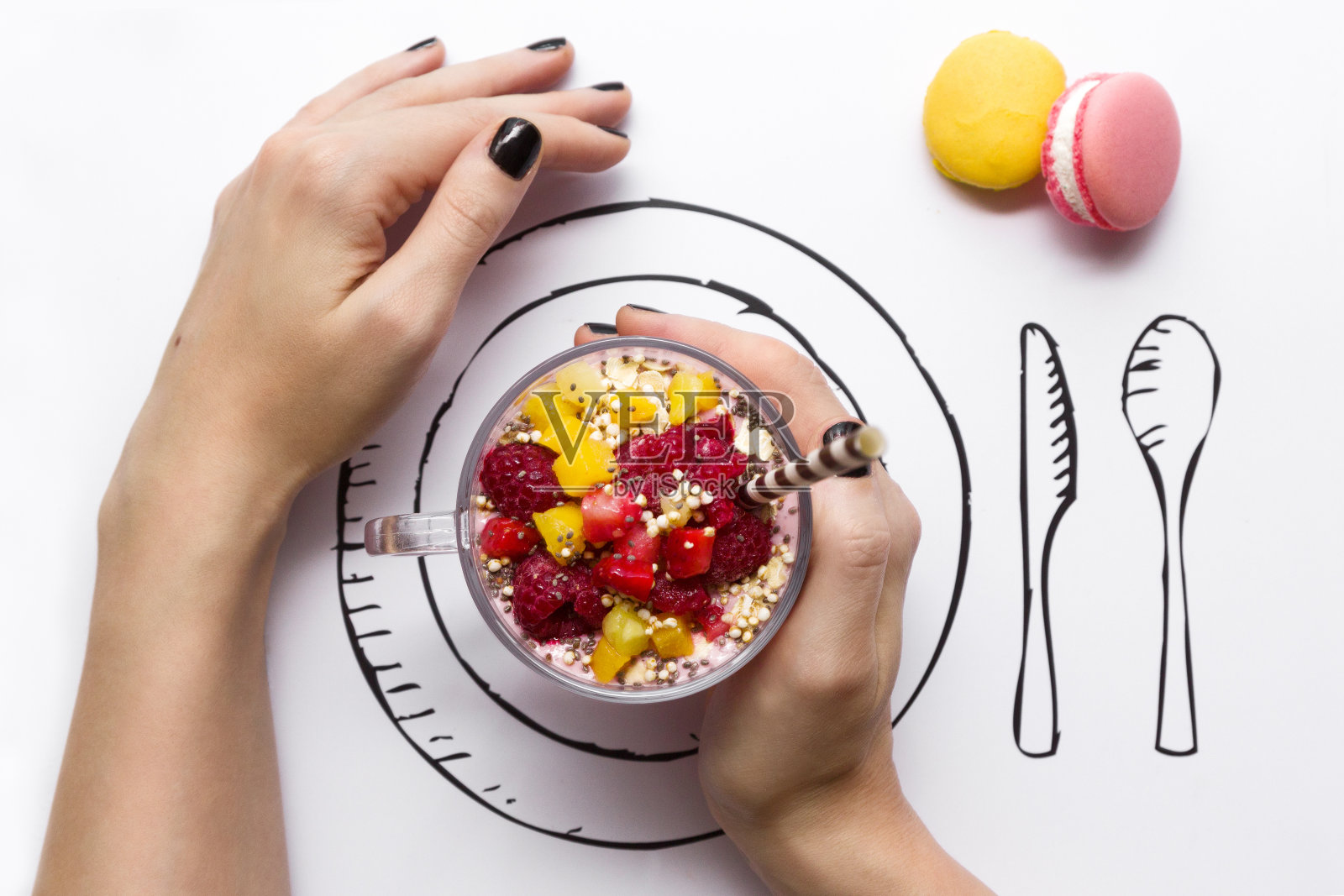 涂着黑色指甲油的女性拿着一杯新鲜的冰沙和彩色马卡龙照片摄影图片