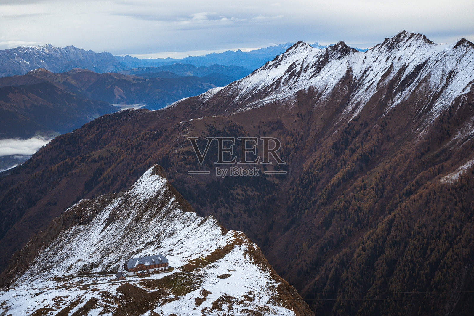 在多云的天空下，高角拍摄了一座建筑在雪山顶上照片摄影图片
