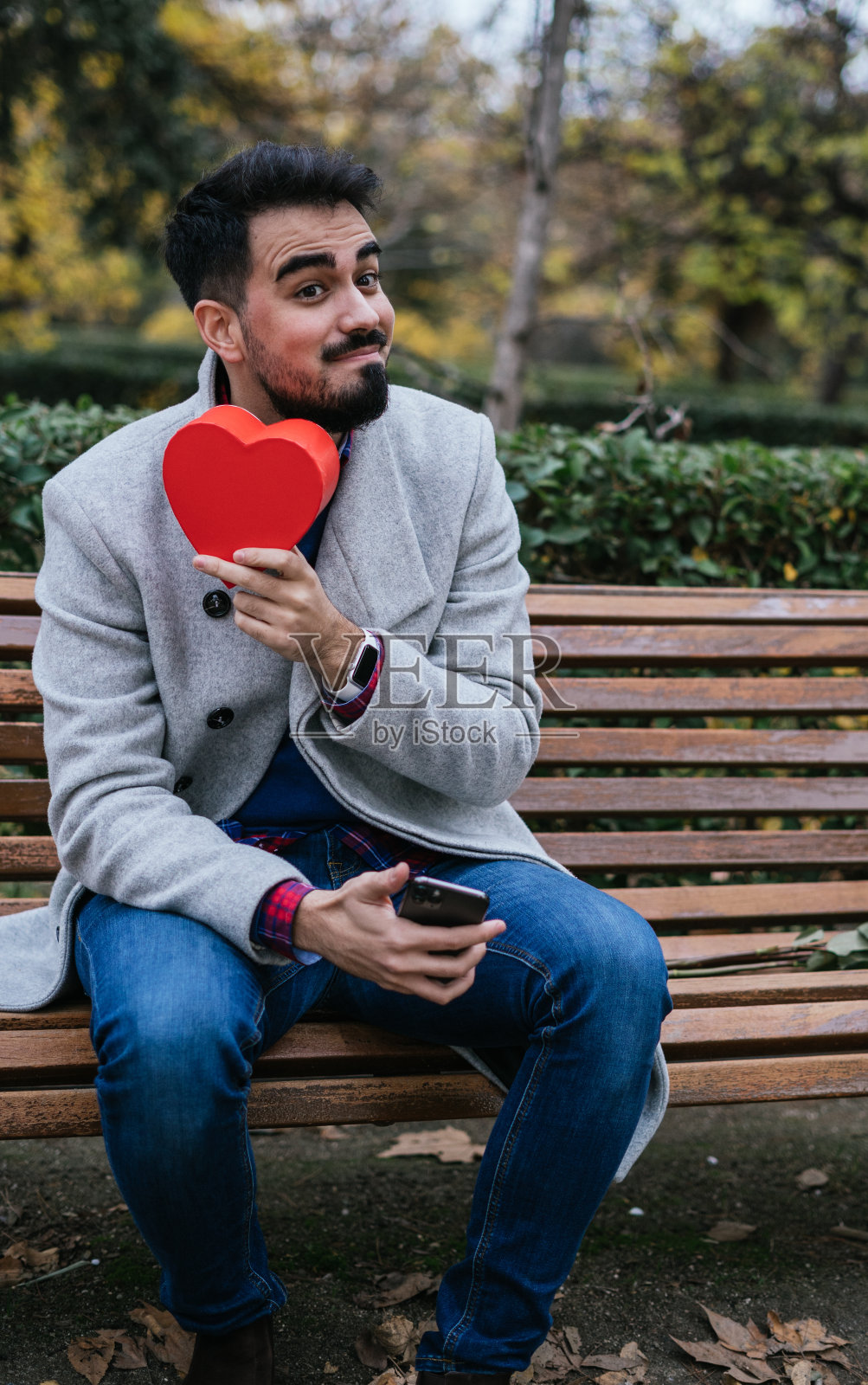 一个男人在户外长凳上拿着一颗红心的垂直特写——情人节概念照片摄影图片