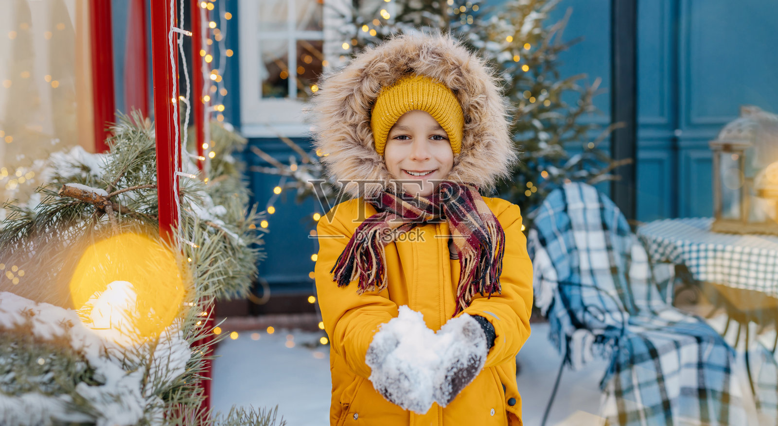在圣诞树和彩灯的背景上，快乐的孩子拿着雪球的肖像。微笑的男孩在户外，在装饰圣诞街。横幅上的寒假主题与空复制空间照片摄影图片