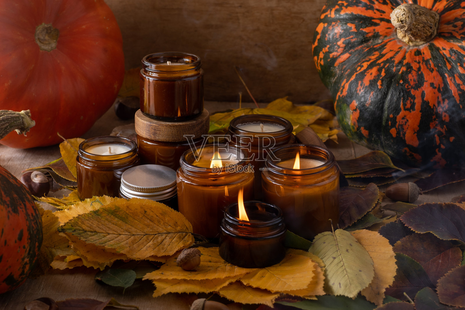 大豆蜡烛在玻璃罐中燃烧。树叶,南瓜。家里舒适。棕色罐子里的蜡烛。光和气味。有香味的手工蜡烛。芳香疗法。秋天的心情。秋天舒适的家居装饰照片摄影图片