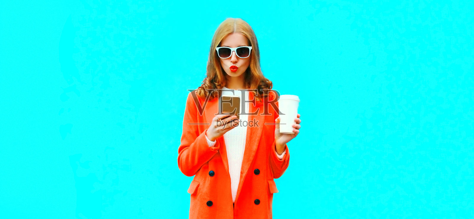 美丽的年轻女子的肖像与智能手机穿着蓝色背景的红色夹克照片摄影图片