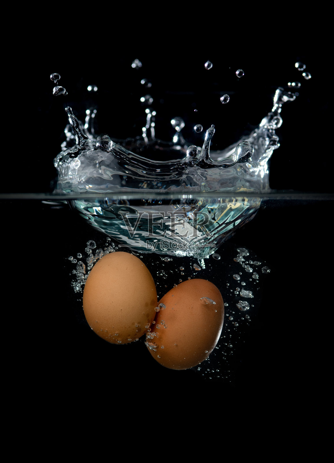 鸡蛋放入水中，溅起的水花孤立在黑色背景上照片摄影图片