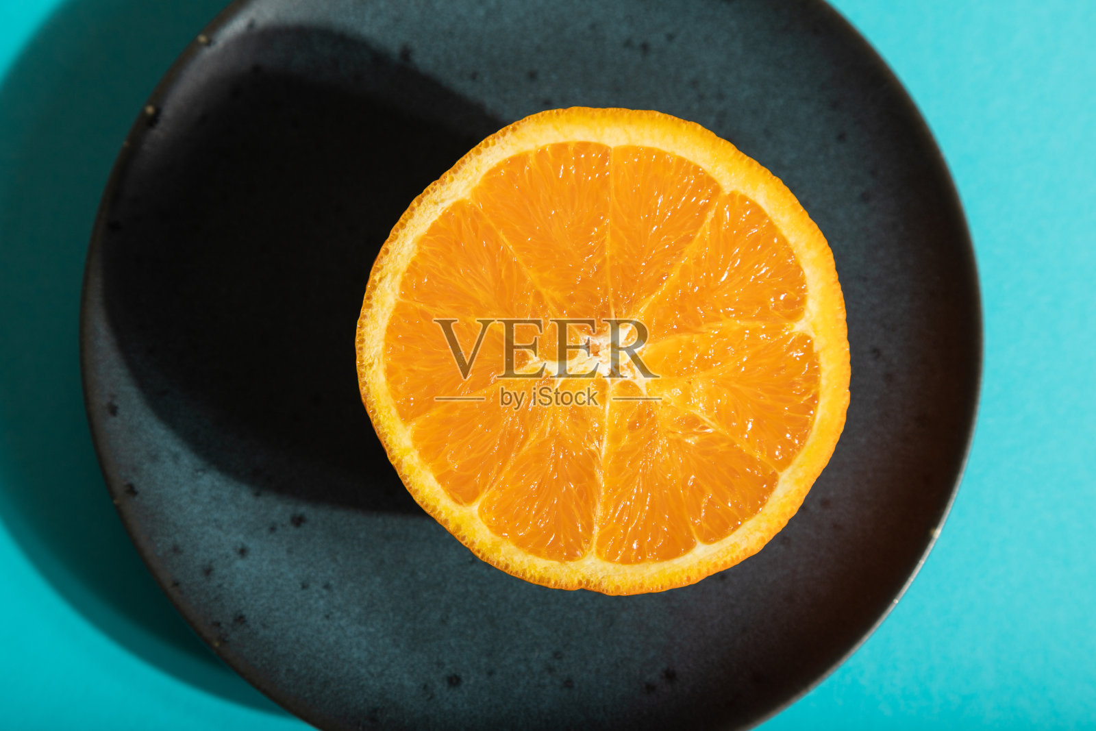 成熟的切橙在蓝色陶瓷盘上蓝色粉彩背景。俯视图，近景，强光。照片摄影图片