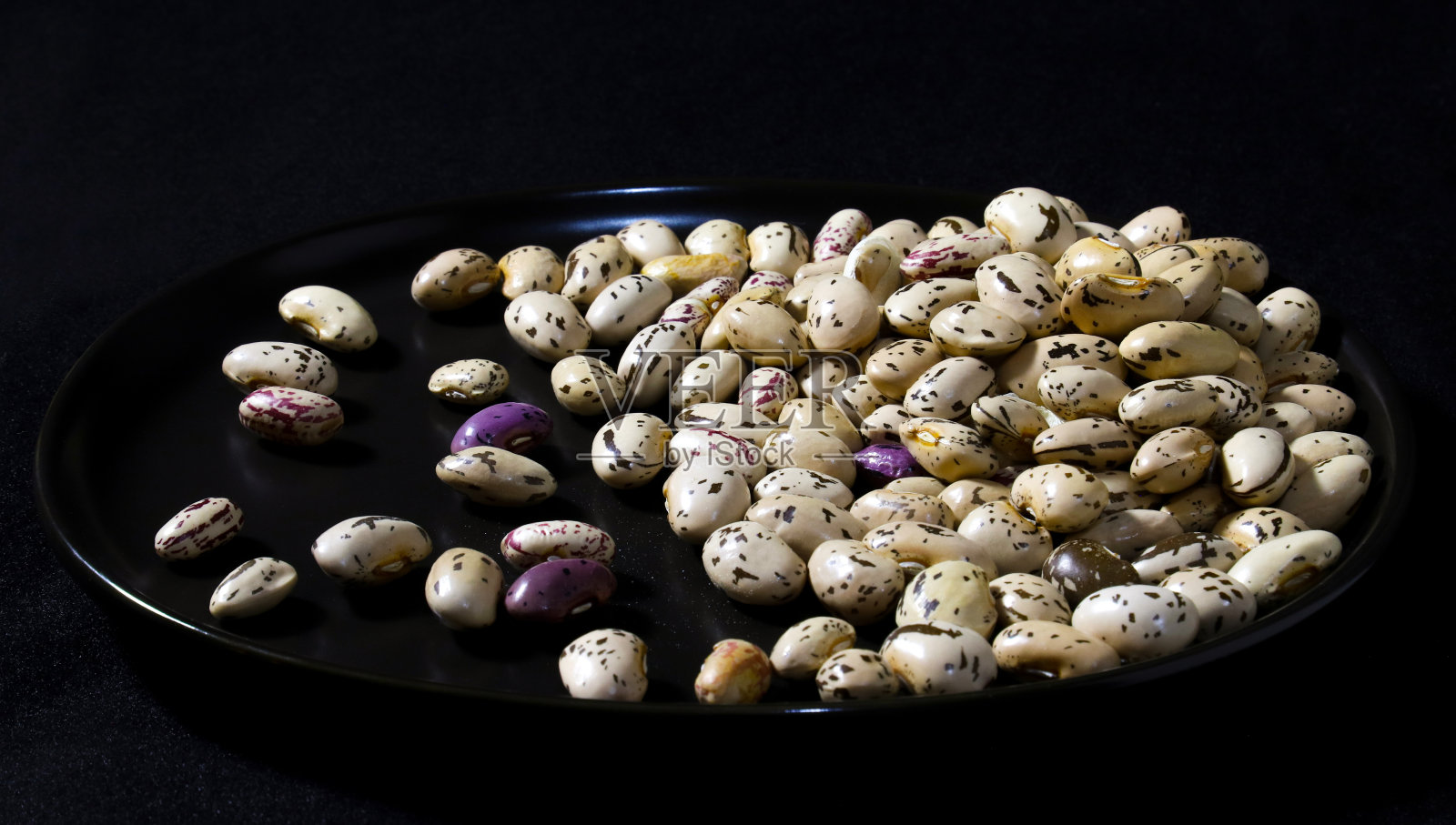 黑色盘子上的杂色平托豆。特写镜头照片摄影图片