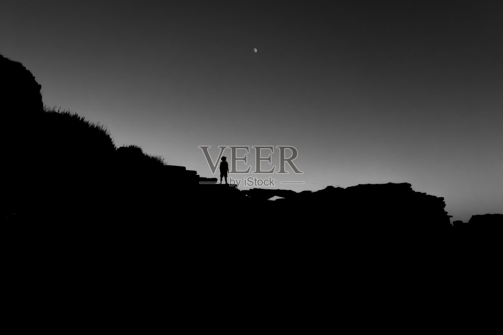 一个人站在大岩石上的剪影的灰色比例镜头照片摄影图片