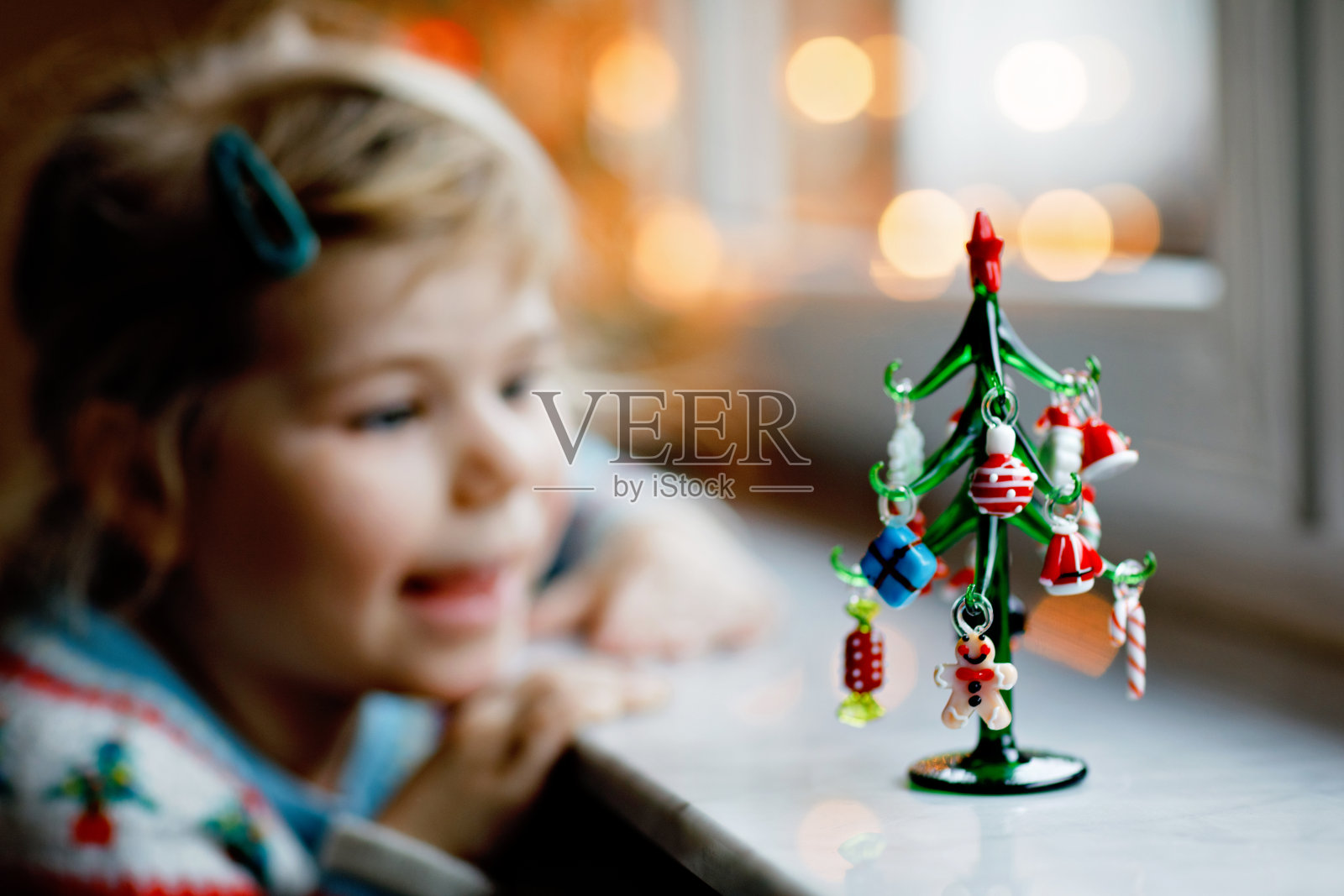 小女孩坐在窗前，用小圣诞玩具装饰小玻璃圣诞树。快乐健康的孩子，庆祝家庭传统节日。可爱的婴儿。照片摄影图片