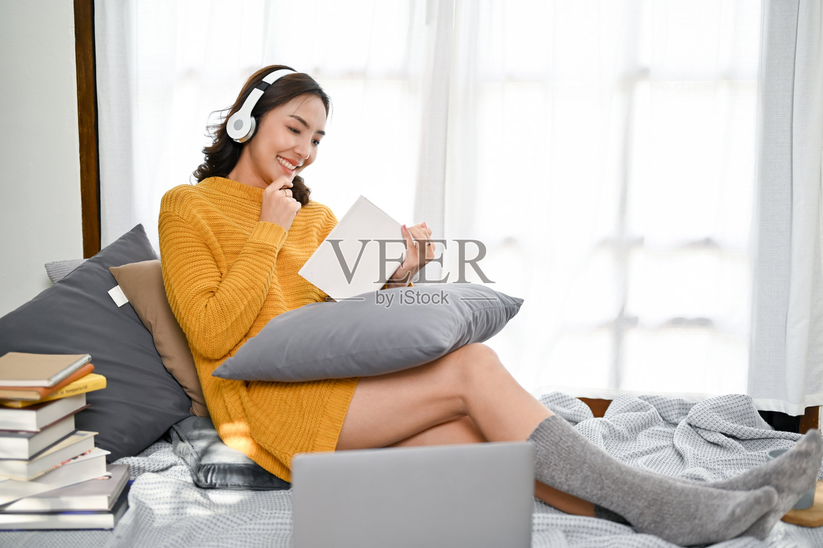 迷人的亚洲女人在她的客厅里一边听音乐一边看书。照片摄影图片