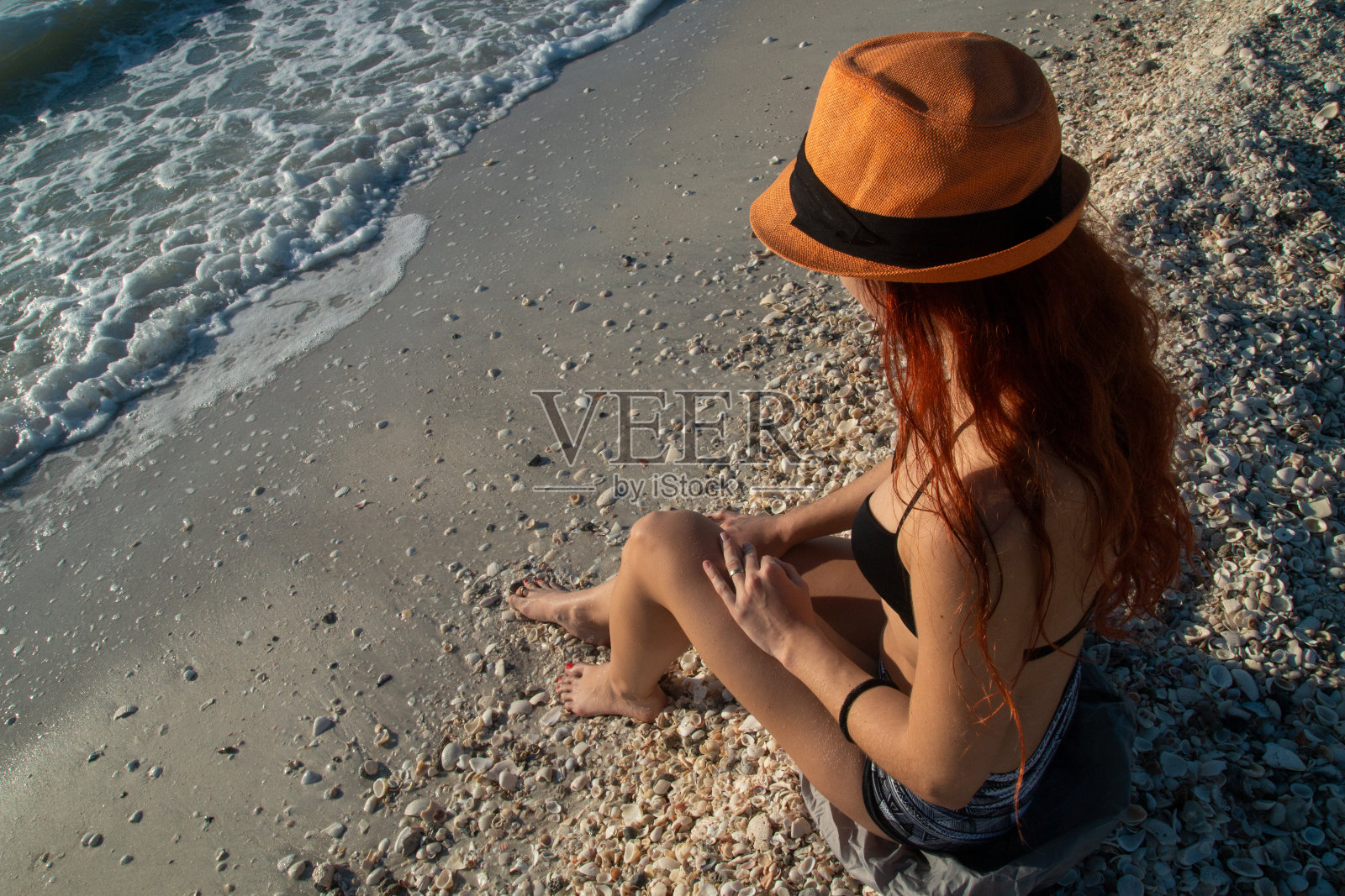 戴着太阳帽的女性身体在海滩上，有很多贝壳，炮轰海滩的Sanibel岛和Captiva，佛罗里达州照片摄影图片