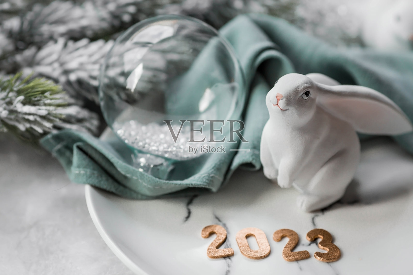 表设置。大理石盘子、绿色餐巾、餐具和一只象征2023年的兔子，背景是冷杉树枝。圣诞快乐，2023年新年和餐厅的概念。照片摄影图片