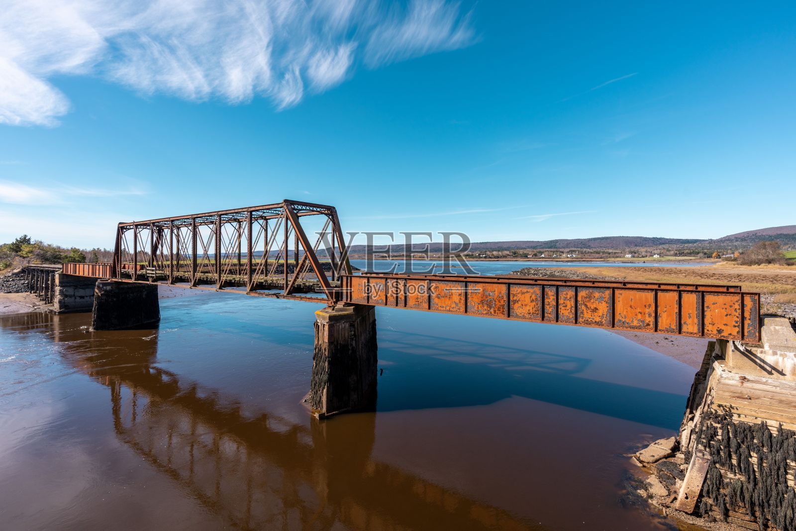 蓝天下连接河岸的锈迹斑斑的桥照片摄影图片