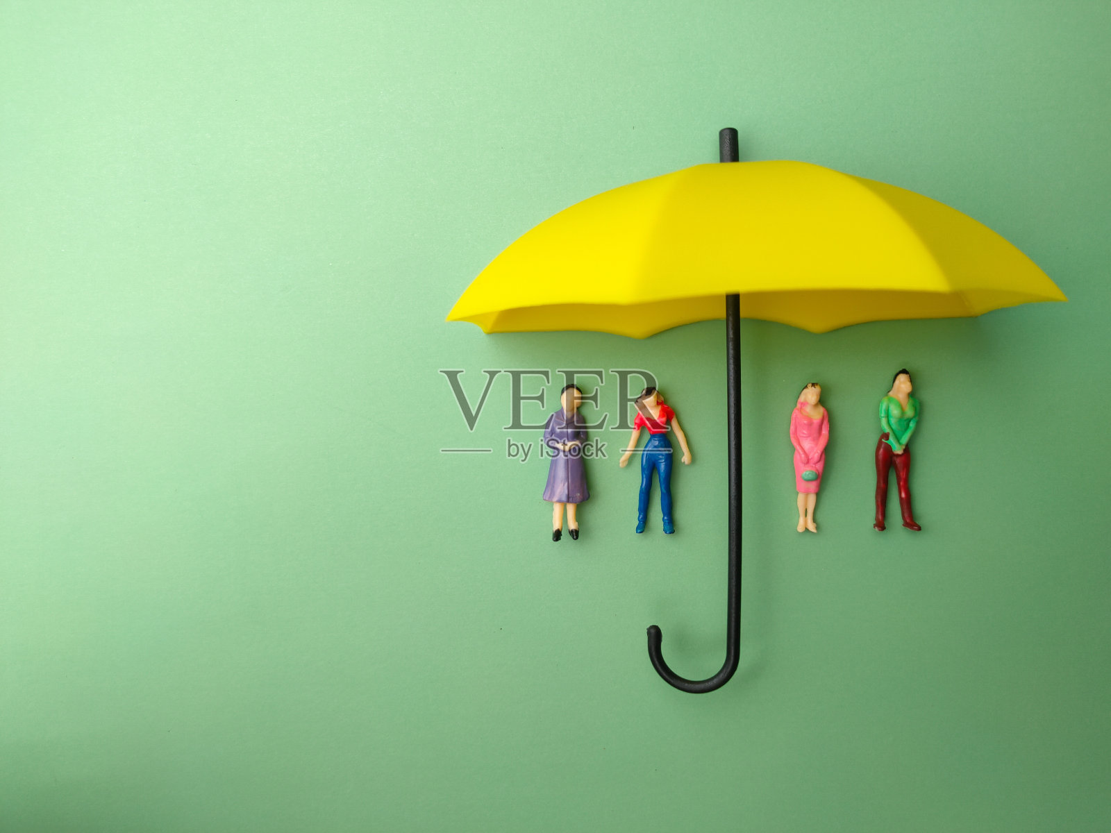 黄色的伞在绿色的背景下保护了一个小女人。自我保护保险的概念。照片摄影图片