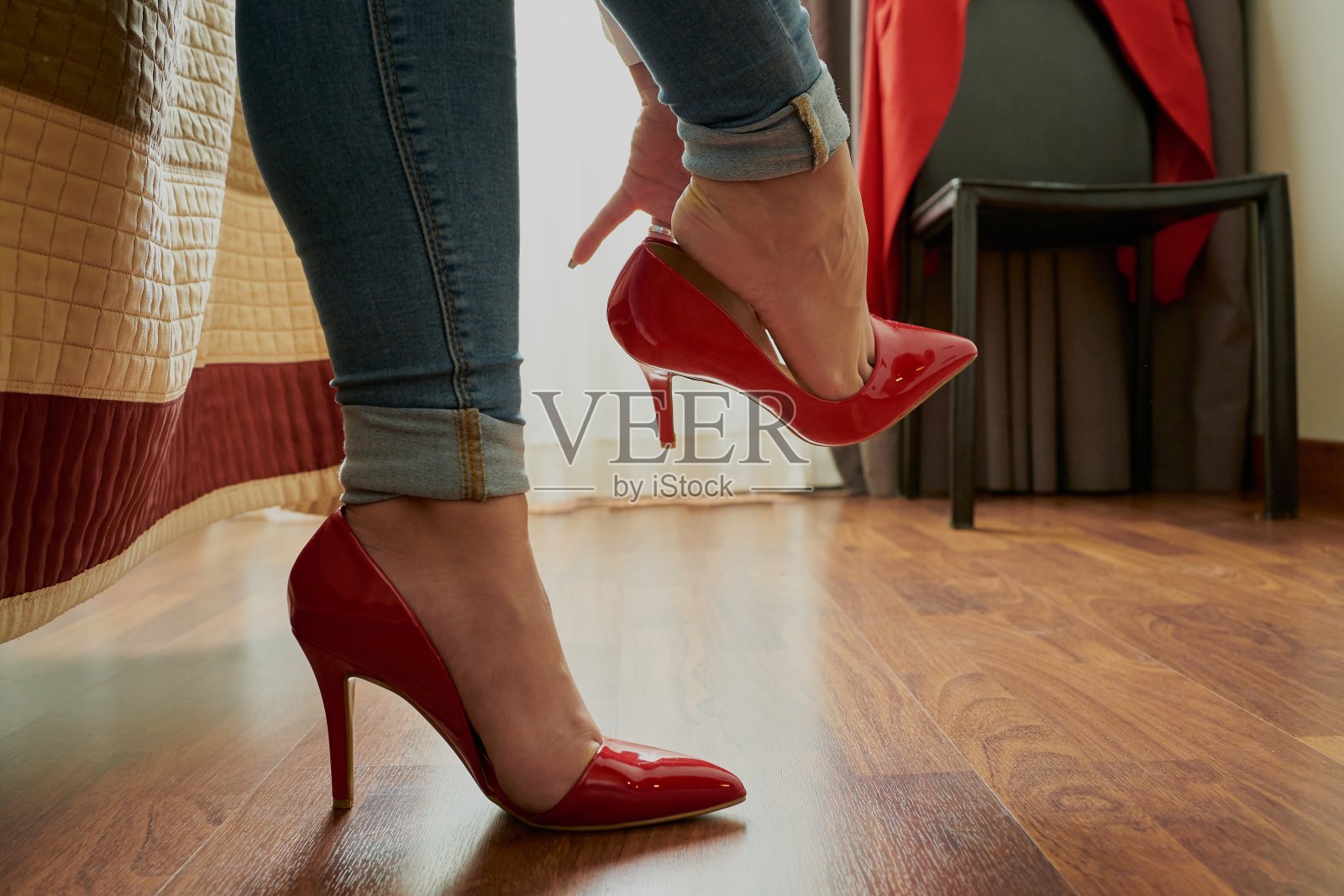 特写的一个女人穿着她的红色高跟鞋，坐在床边照片摄影图片