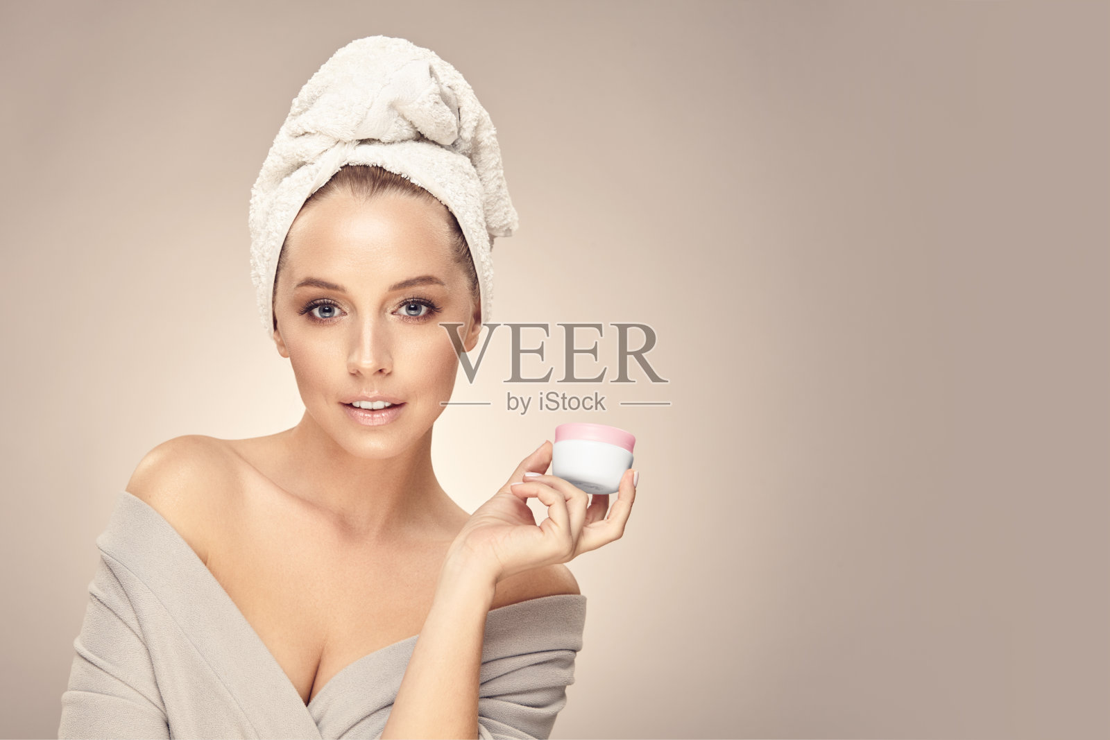 女模特沐浴后抱着她的脸附近的自然生态安全霜在米色隔离，接近肖像与自由复制空间。照片摄影图片