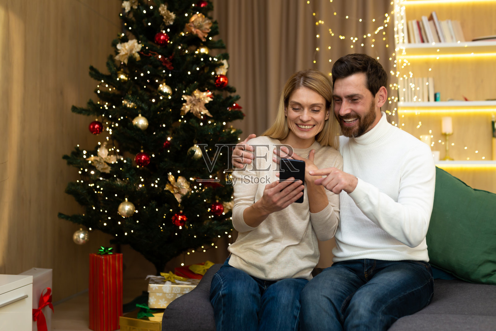 已婚夫妇在假日网上选择圣诞礼物。幸福恩爱的夫妻坐在红彤彤的新年树旁照片摄影图片