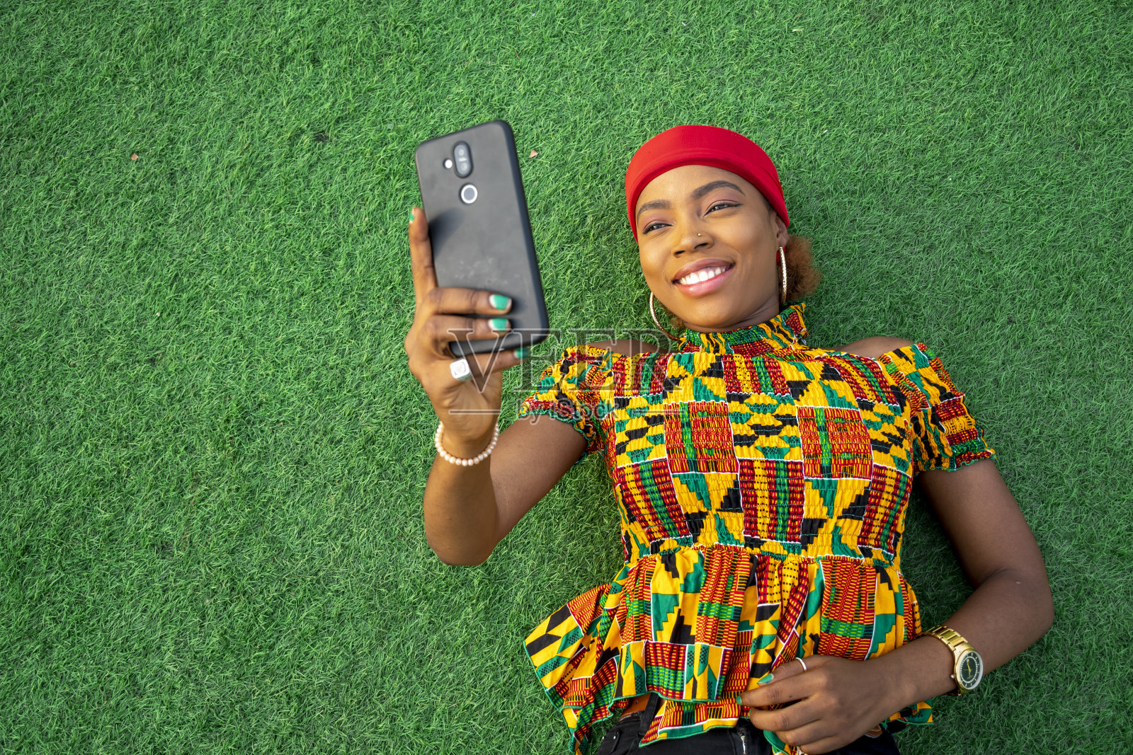 美丽的年轻黑人女性躺在公园的地板上用她的手机照片摄影图片