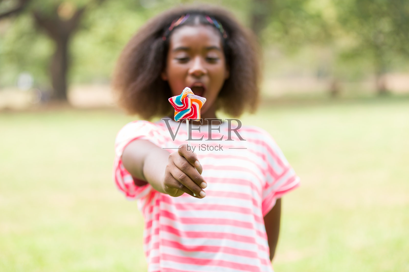非裔美国女孩在公园里玩五颜六色的棒棒糖的画像。快乐的小女孩与棒棒糖户外照片摄影图片
