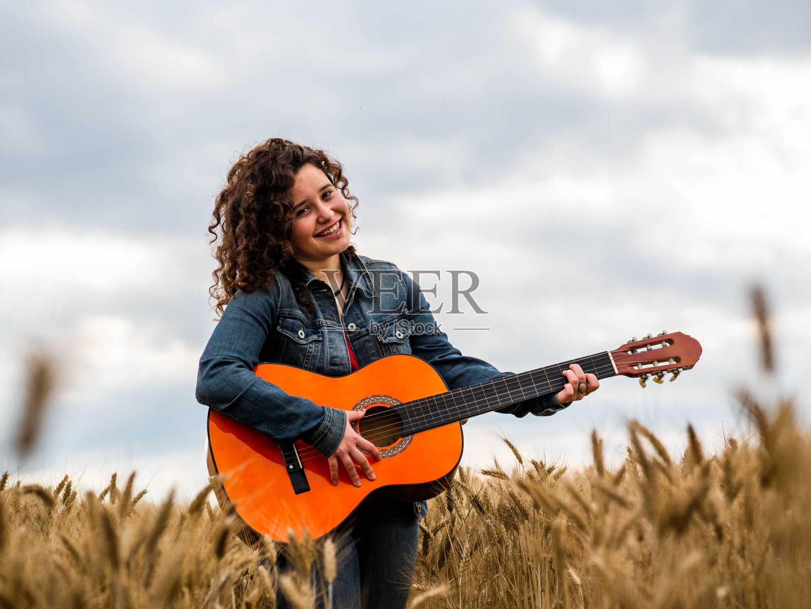 浅聚焦镜头一个美丽的年轻女子在麦田弹吉他照片摄影图片