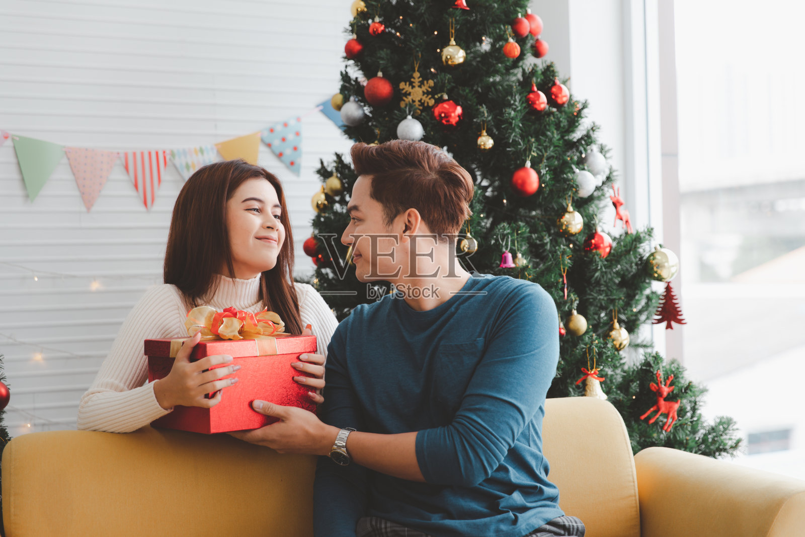 在新年和圣诞节期间，一个男人在装饰着圣诞树的客厅里给一个女人送礼物照片摄影图片