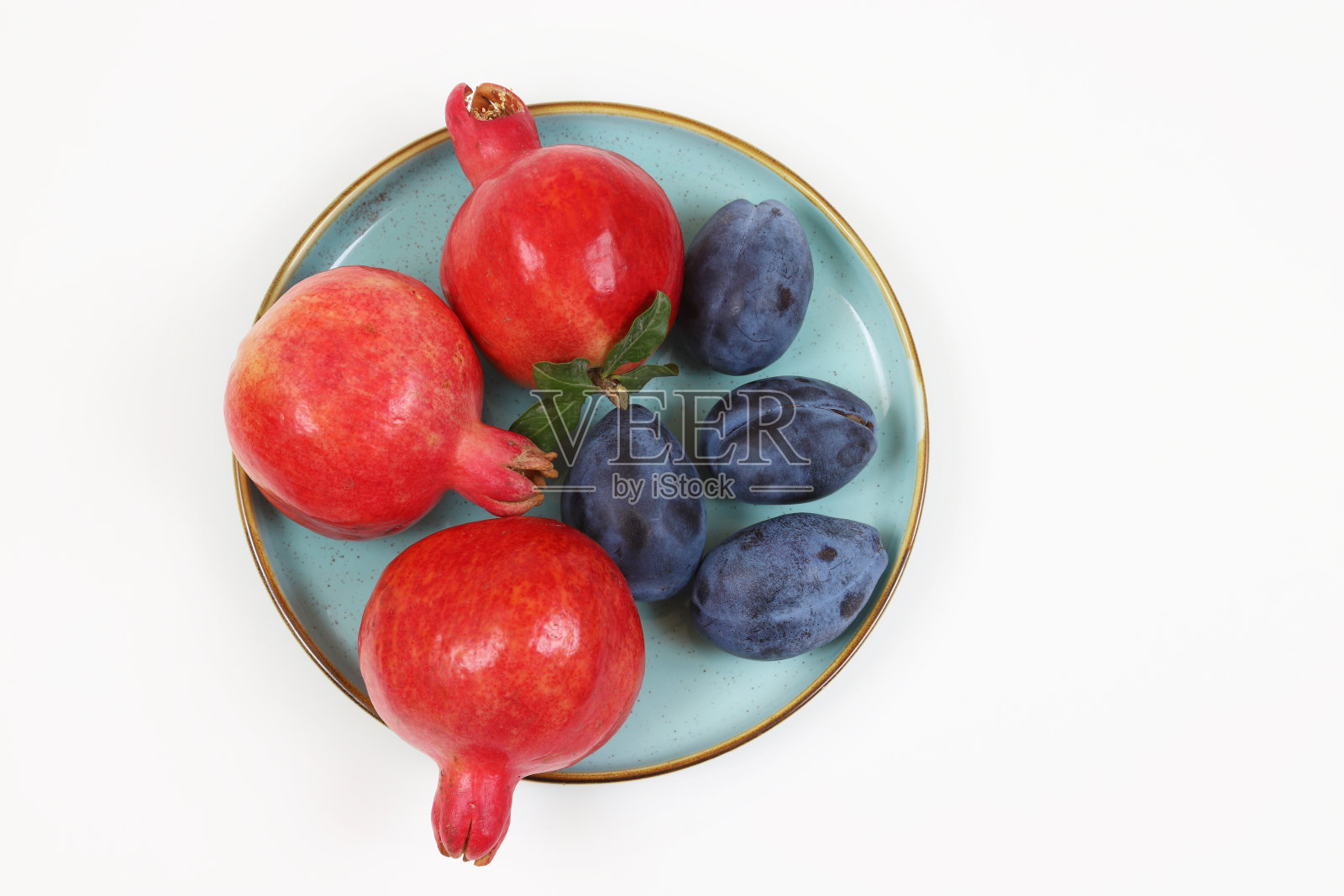 白色的桌子上放着成熟的红石榴和黑李子。浅景深照片摄影图片