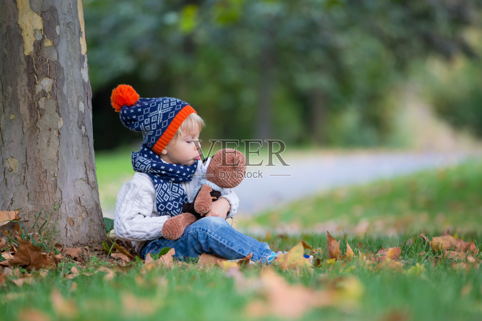 蹒跚学步的孩子，男孩，在秋天的公园里玩编织的amigurumi泰迪熊照片摄影图片