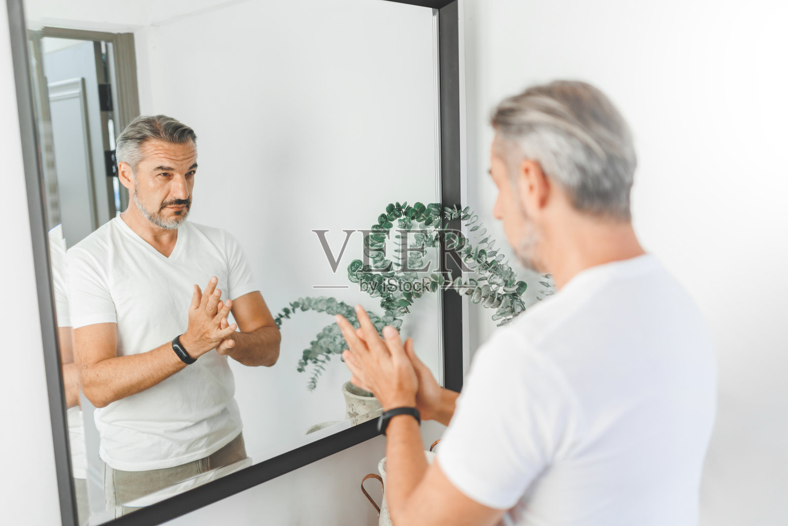 成熟的成年男子检查自己的头发，看着镜子照片摄影图片