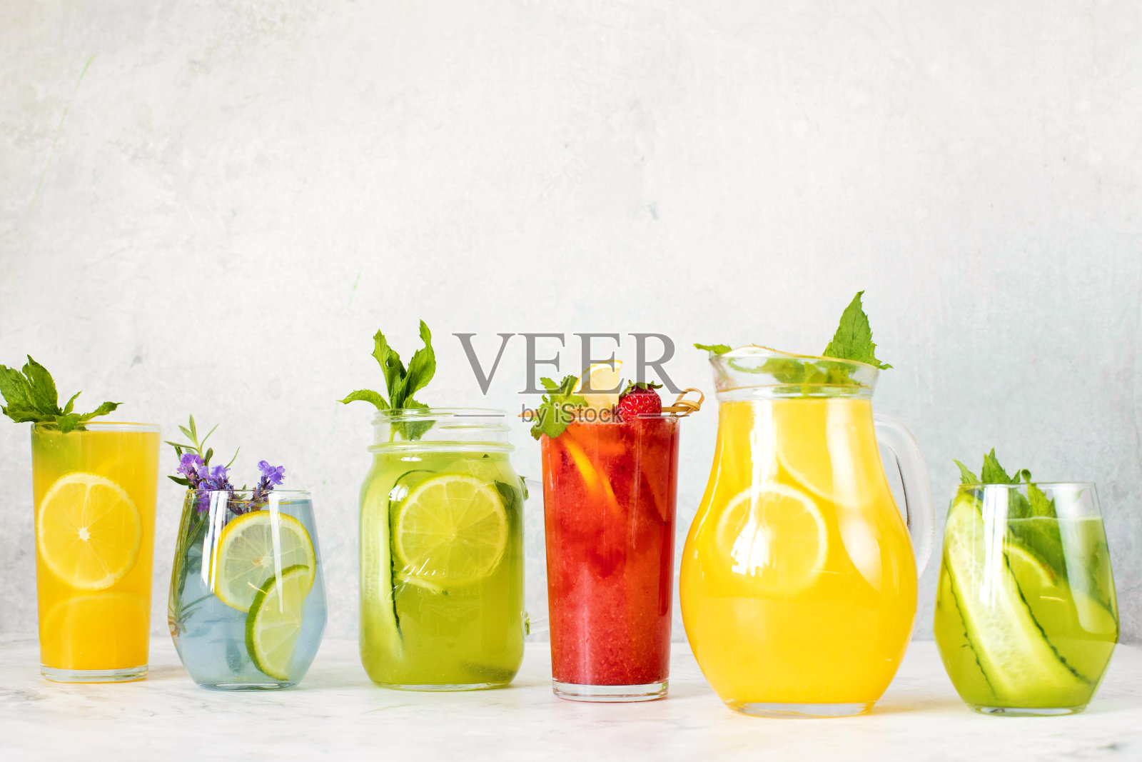 柠檬水是不同的薰衣草，黄瓜，酸橙和薄荷，柠檬，草莓在灰色的背景。照片摄影图片