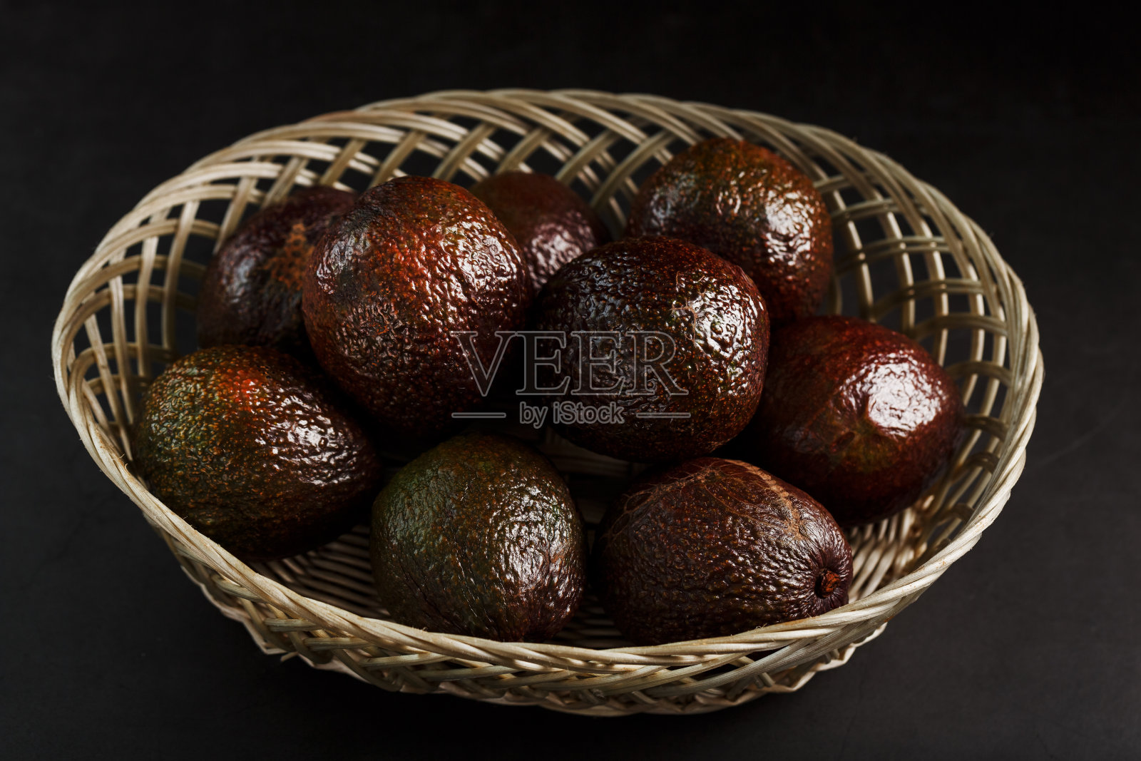 成熟的牛油果装在篮子里，放在黑色的桌子上，还有一个切好的水果和一块果核。照片摄影图片