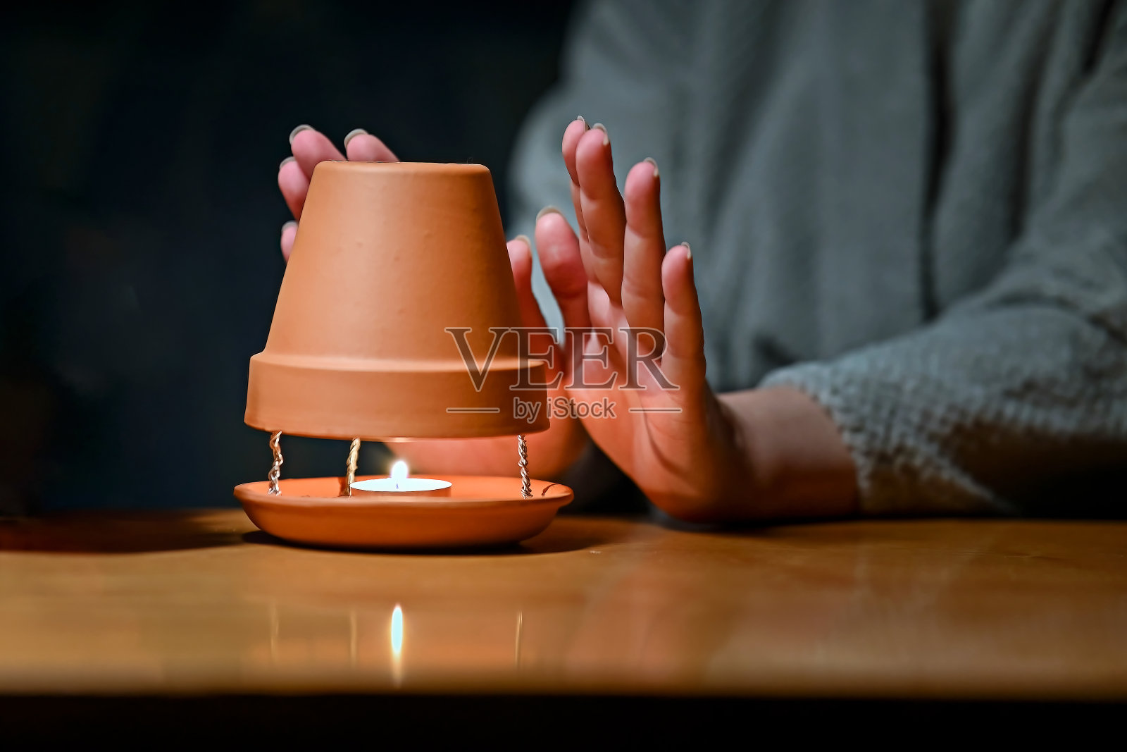 一名妇女在黑暗中用蜡烛和锅自制加热器取暖。照片摄影图片