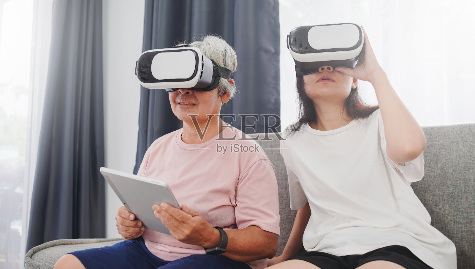 一位拿着平板电脑的亚洲女性和她的女儿戴着VR眼镜、虚拟现实概念和元世界，惊呆了。照片摄影图片