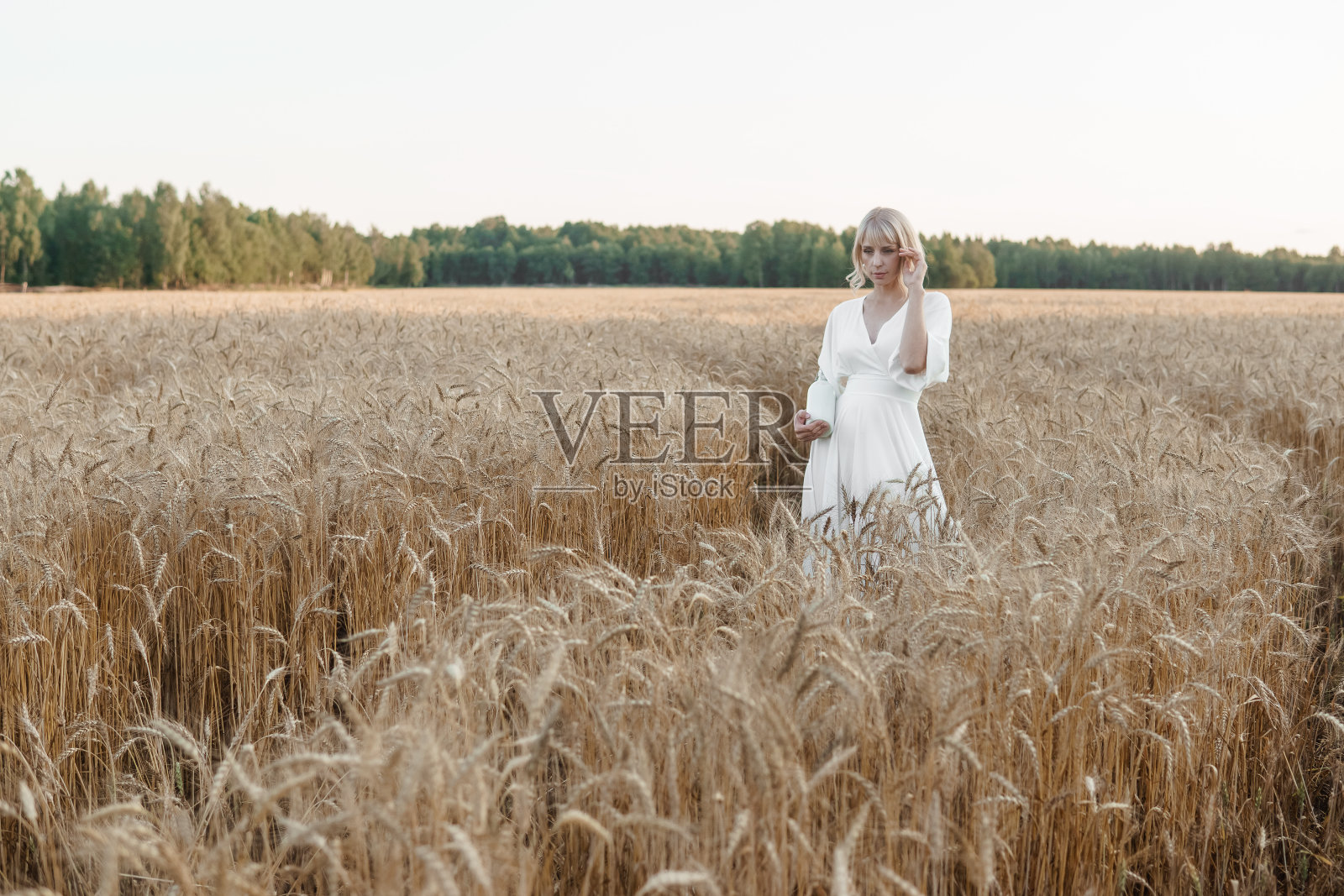 一位身穿白色长裙的金发女郎走在麦田里。婚礼的概念和在大自然中行走照片摄影图片