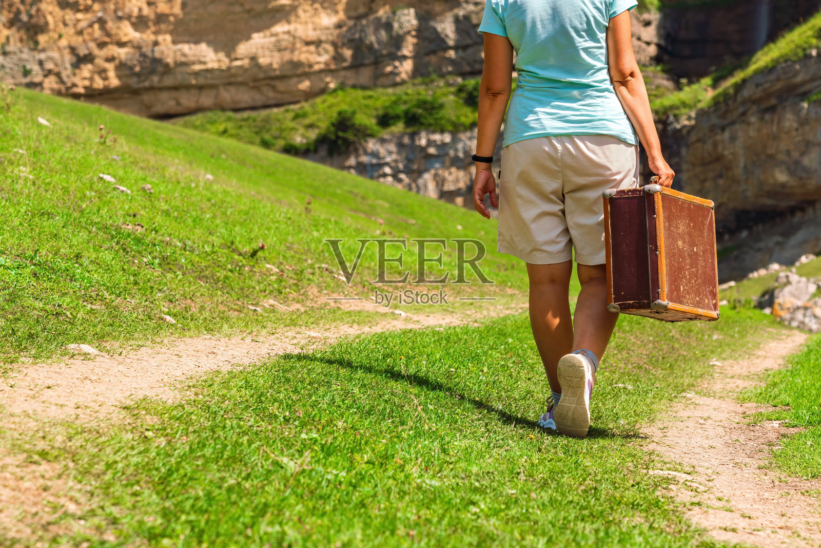 一个提着行李箱的女孩走在山里的土路上。孤独女人的有趣旅程照片摄影图片