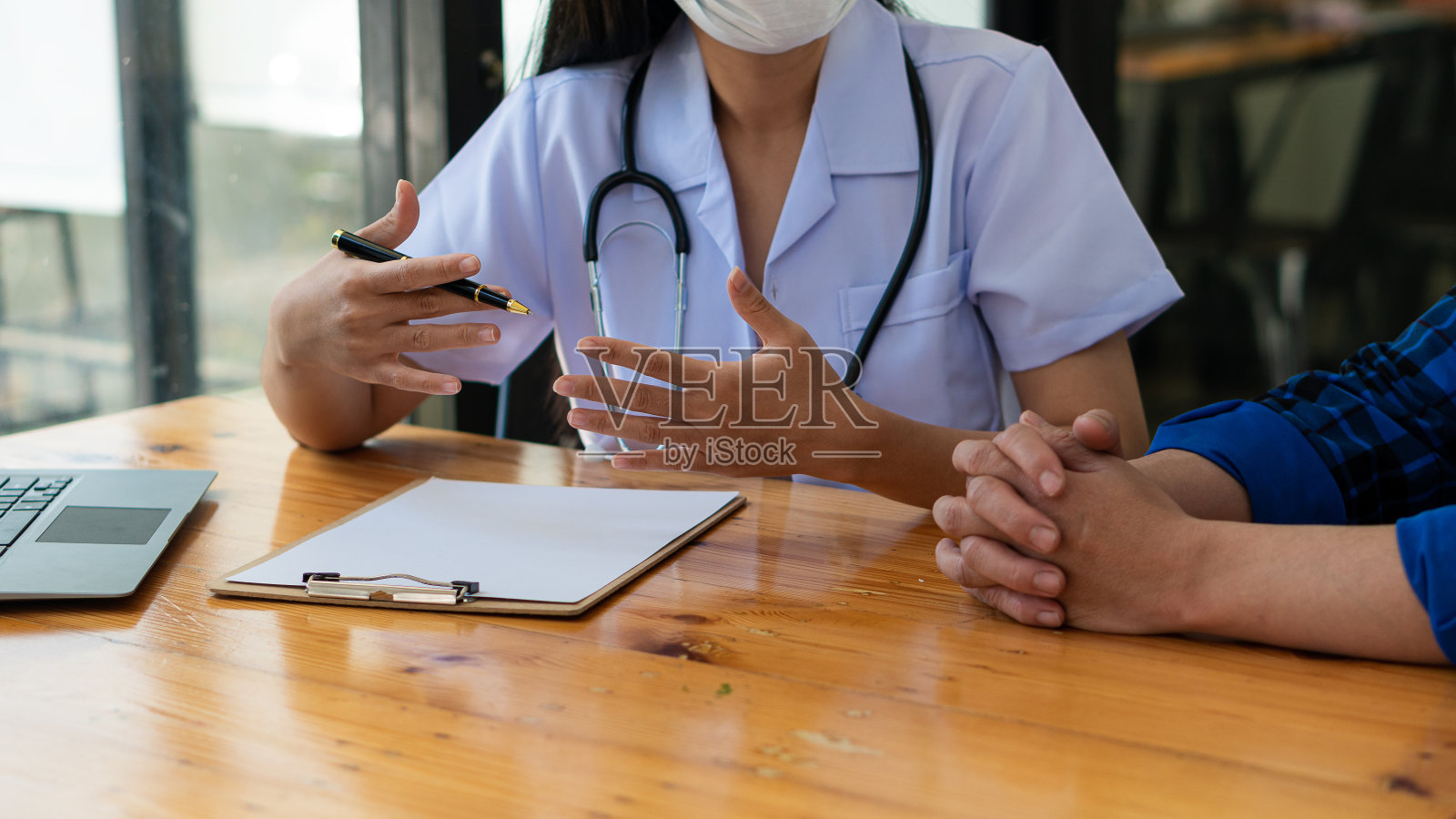 医生和病人坐在一起，和病人谈论药物。在医院靠窗的桌子旁女医生说话，检查着小病人，医生做着笔记。照片摄影图片